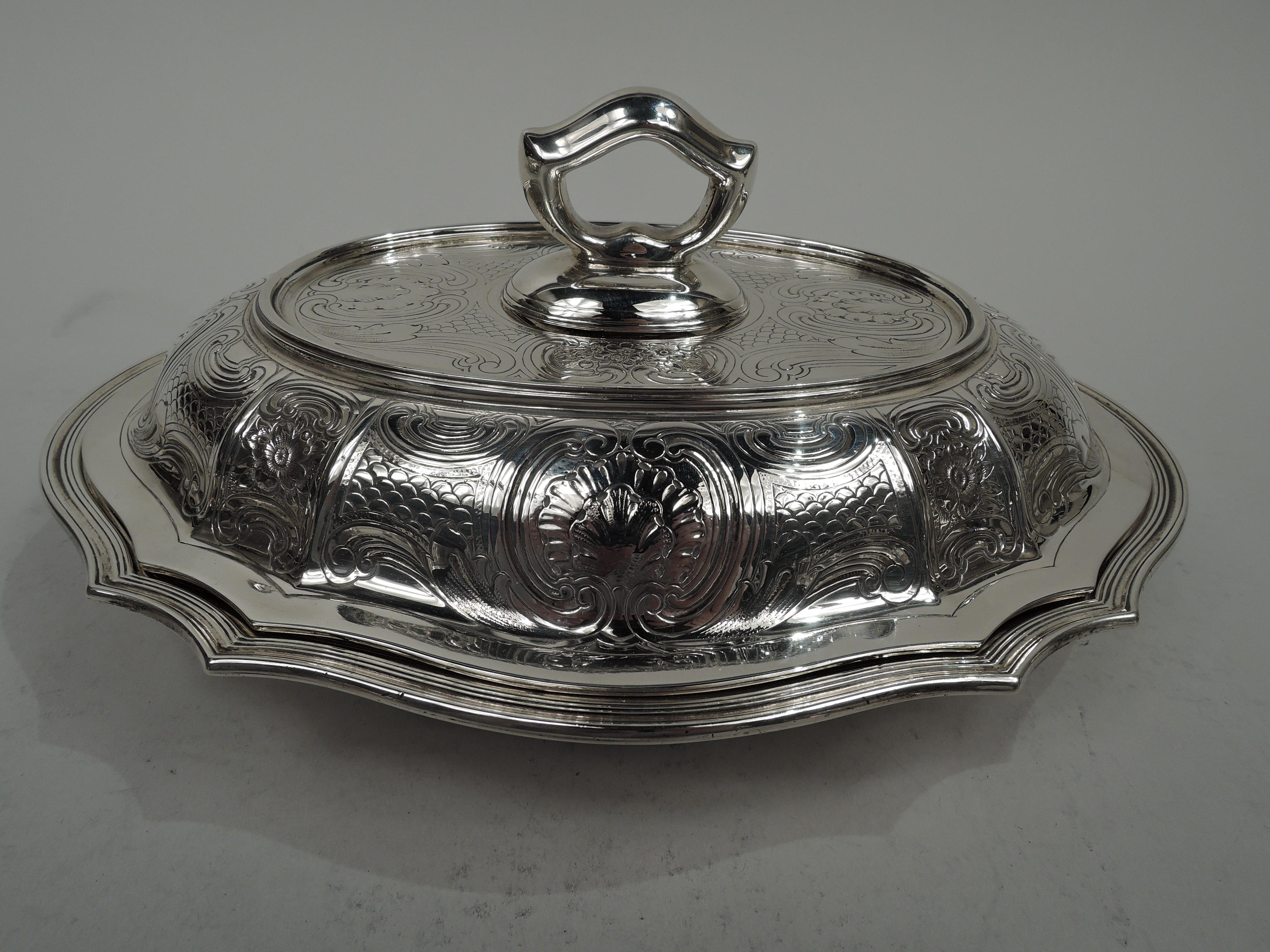 Ciotola classica in argento edoardiano moderno. Prodotto da Tiffany & Co. a New York, 1910 circa. Ovale e serpeggiante, con lati affusolati e bordo ribattuto. Coperchio rialzato con lati affusolati e bordo liscio e piatto. Fitte incisioni di volute,