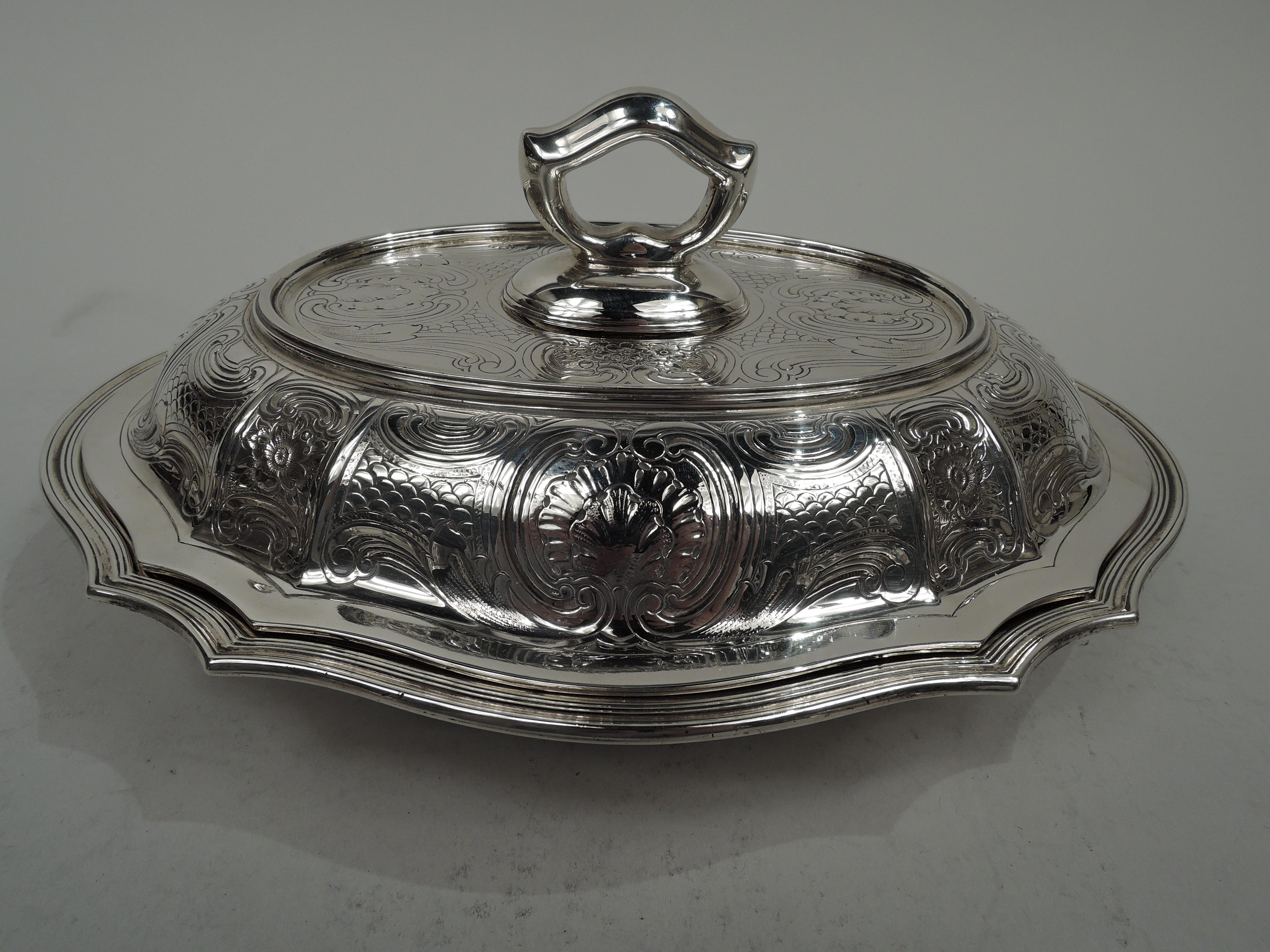 Edwardian Modern Classical sterling silver serving bowl. Made by Tiffany & Co. in New York, ca 1910. Oval and serpentine with tapering sides and reeded rim. Cover raised with tapering sides and plain and flat rim. Dense engraved scrolls, flowers,