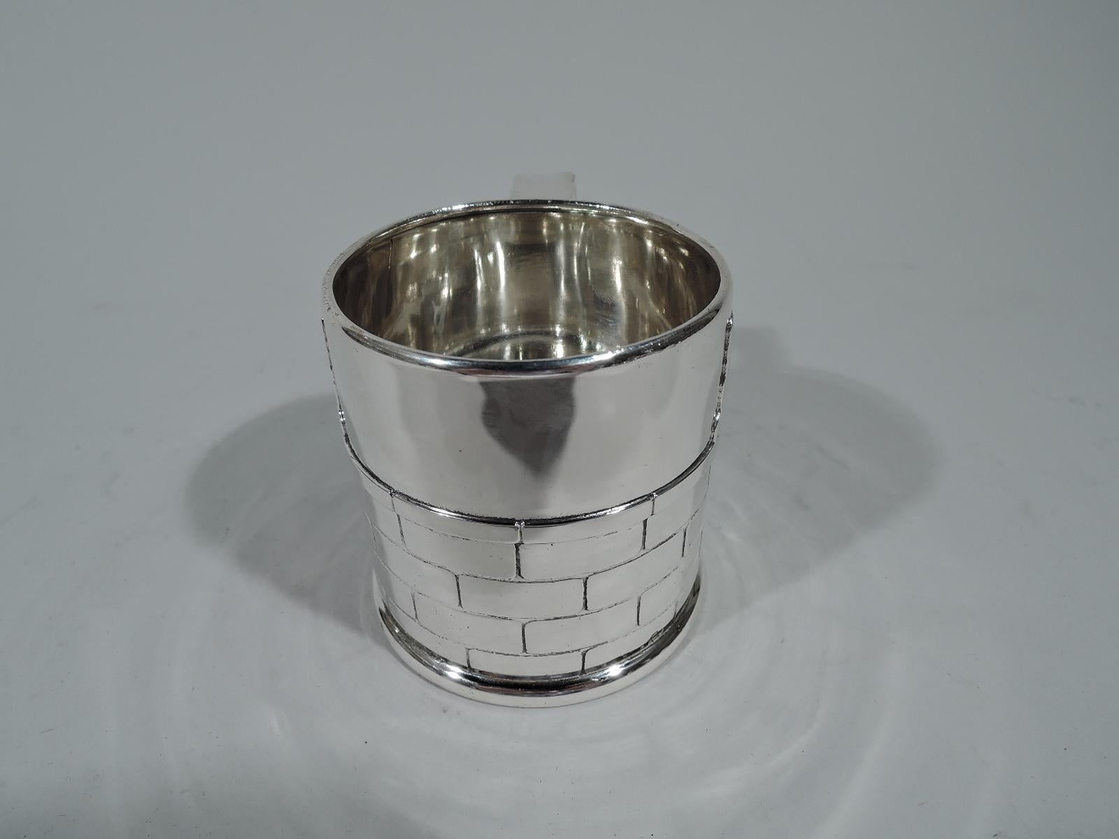 Edwardian sterling silver baby cup with peekaboo kitty cat. Made by Tiffany & Co. in New York. Drum form with molded base and bracket handle. Two heads with pointy ears and fat paws peep above a brick wall. Fine evocation of the intense and