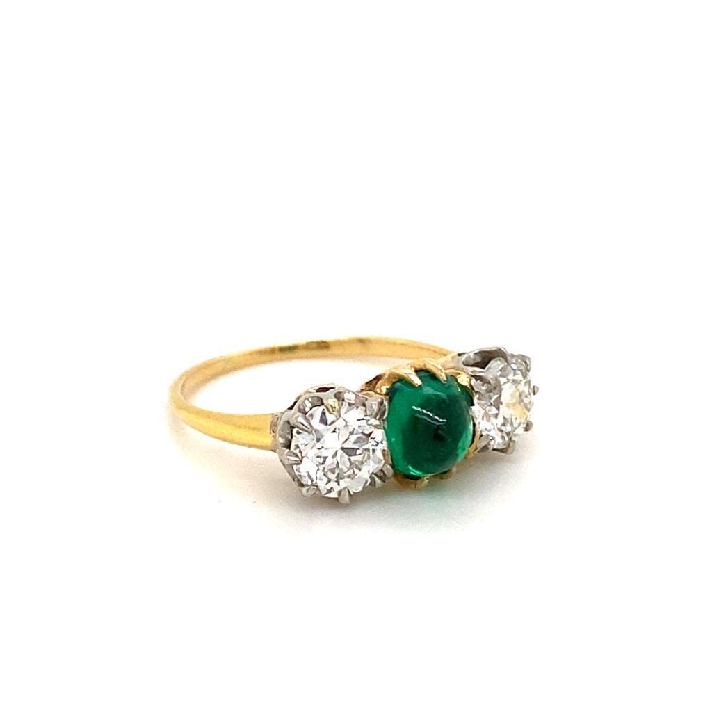 A Tiffany & Co emerald and diamond three stone engagement ring in 18 karat yellow gold, circa 2012.

This classic ring is centrally set with a round cabochon emerald in a simple four claw 18 karat yellow gold setting, which enhances its deep green