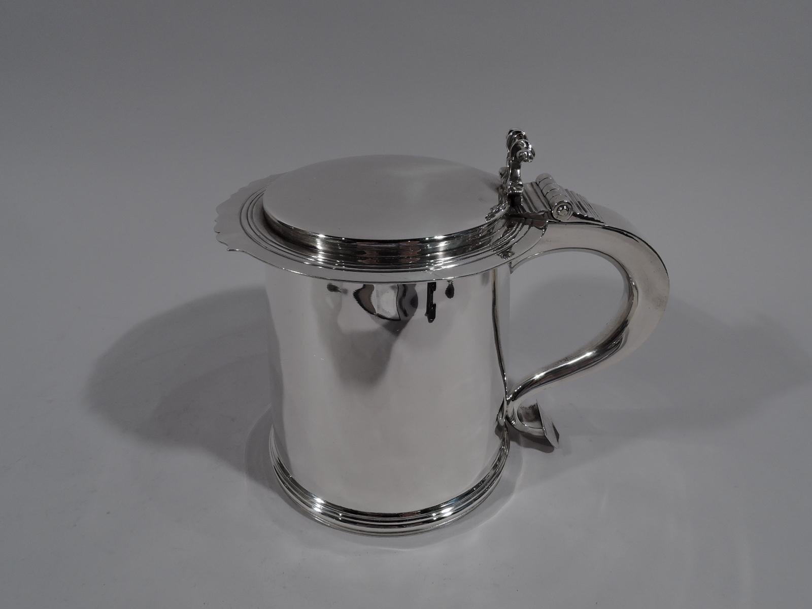 English sterling silver tankard, 1955. Retailed by Tiffany & Co. in England. Drum-form with gently upward tapering sides, molded base, and s-scroll handle with ornamental thumb rest. Cover flat, raised, and overhanging with tooled bands and
