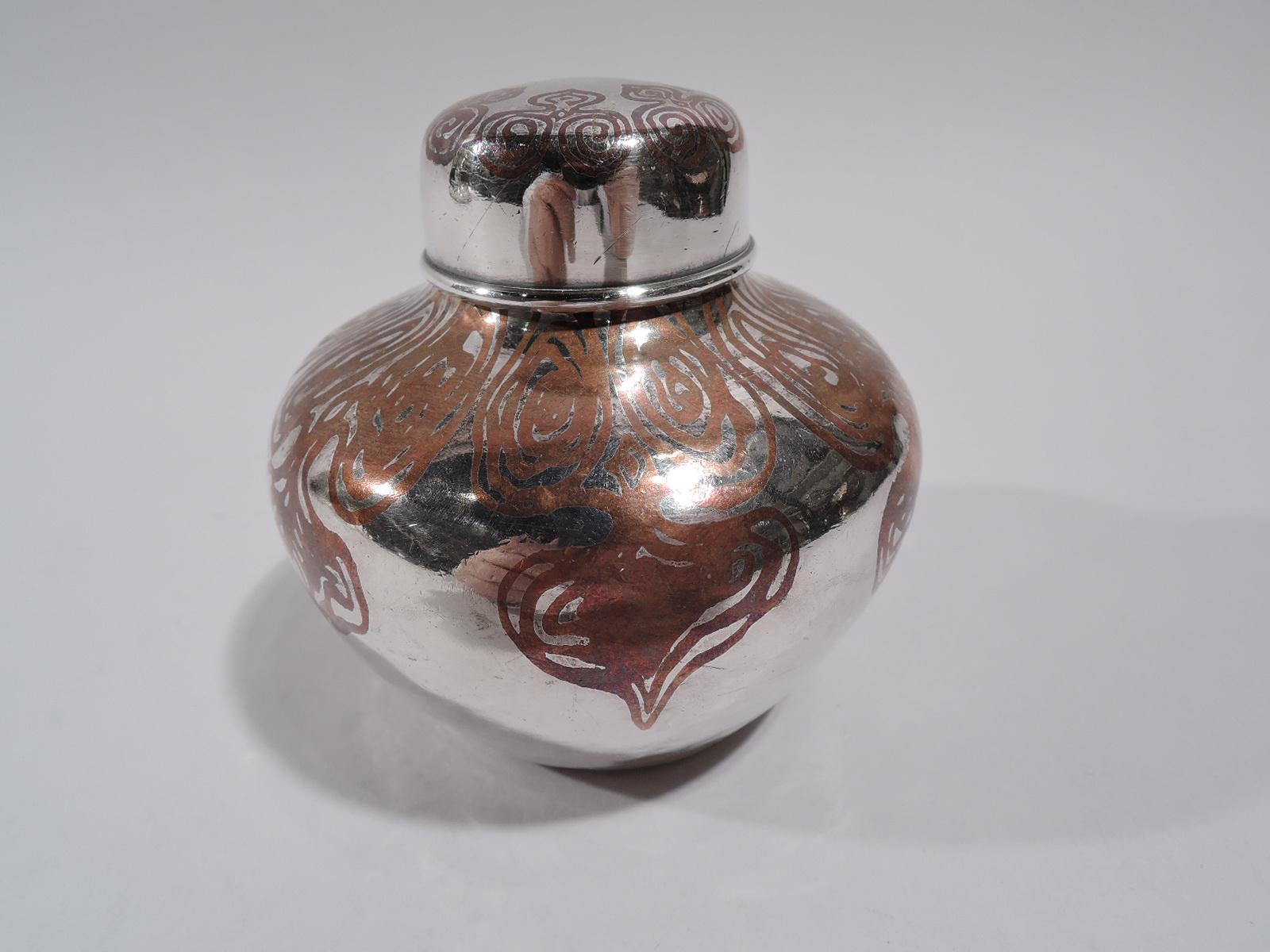 Exotic mixed metal tea caddy. Made by Tiffany & Co. in New York, circa 1910. Sterling silver ginger-jar with squat and tapering sides, short neck, and snug-fitting cover. Copper ornament with irregular scrollwork. Fully marked including pattern no.
