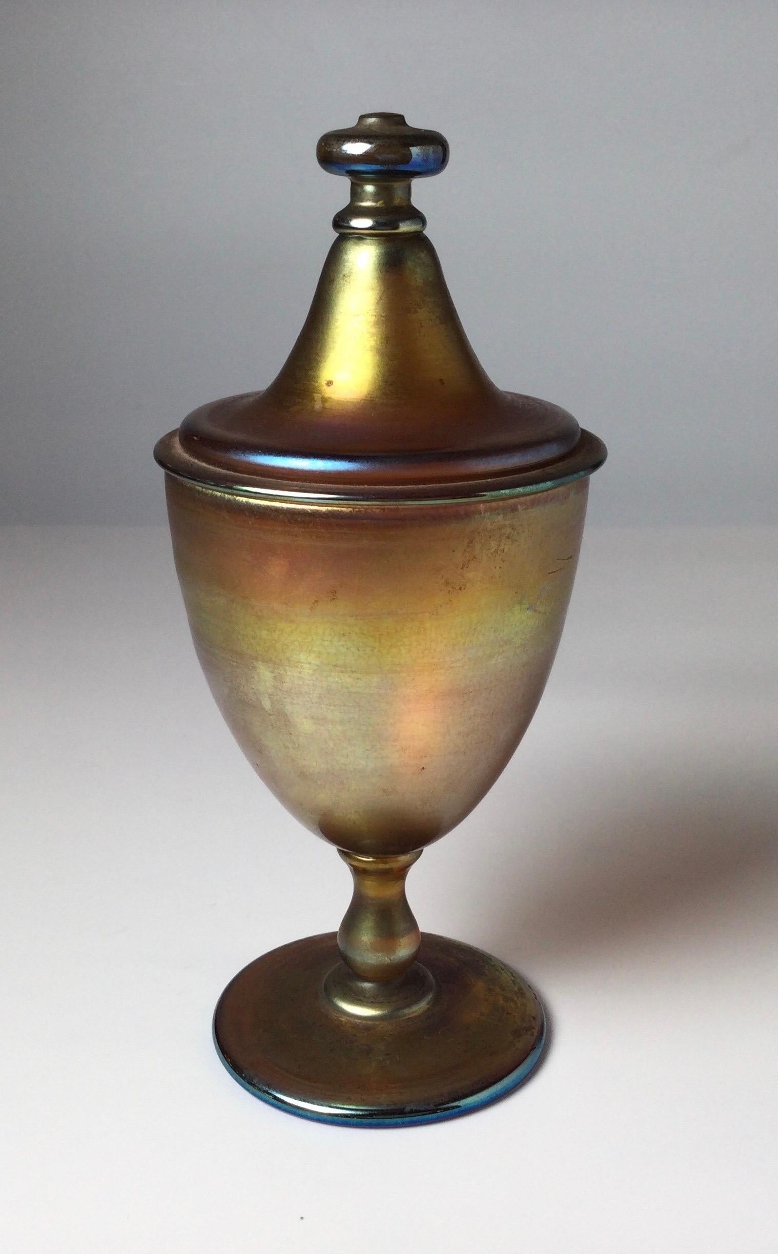 Signed Louis Comfort Tiffany favrille glass footed compote. The classic urn shape on pedestal base with raised cover with flattened knop. The glass in shades of deep gold, pumpkin, pink and blue iridescence. Clearly signed on bottom. Provenance- Mr.
