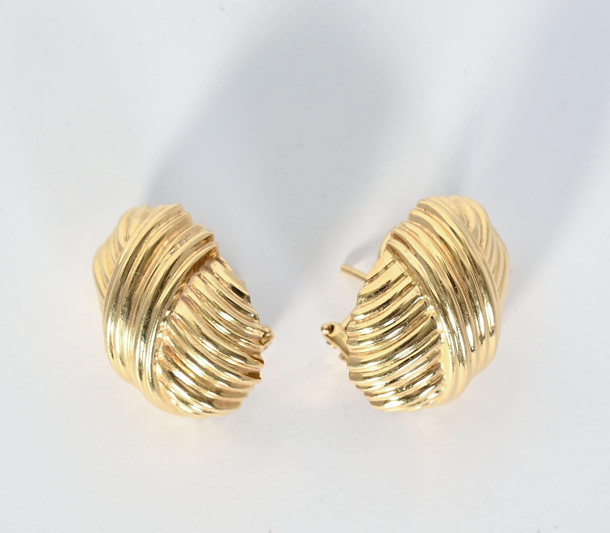 Tailored 18 karat gold earrings by Tiffany. The oval earring has a ribbed surface over which a diagonal of the same texture creates added interest. The earrings are half an inch wide and three quarters of an inch long. Backs are posts and clips.