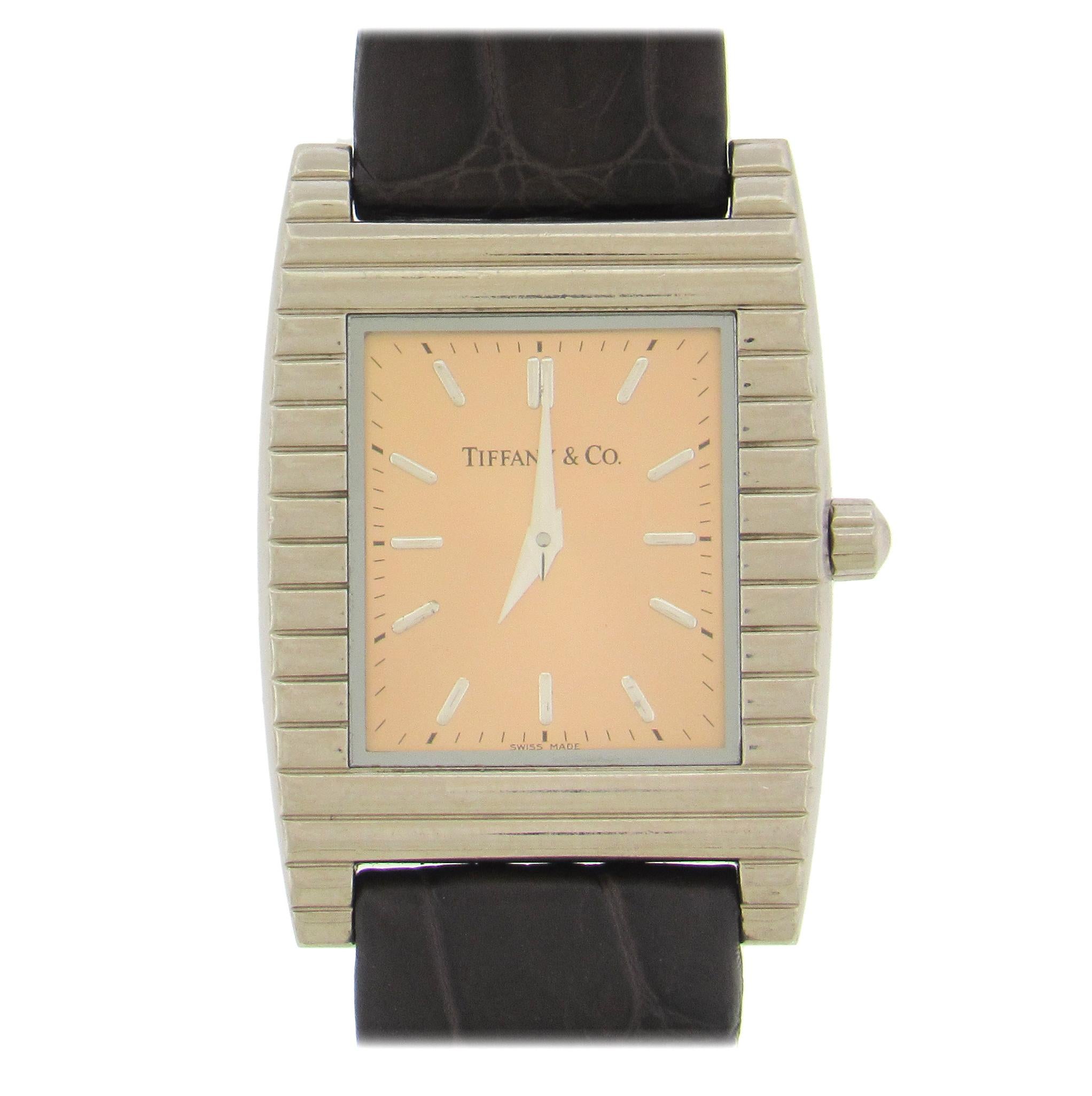 Elegant 18K white gold Tiffany quartz wristwatch, circa 2000, has a 28mm x 39mm case with snapback, stylized corrugated bezel, with matching Tiffan 18K buckle, salmon dial with applied white gold hour markers and dauphine hands. Quartz movement.