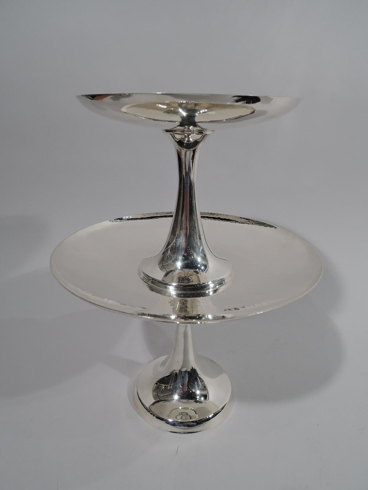 Mid-Century Modern sterling silver cake stand. Made by Tiffany & Co. in New York. This stand comprises two compotes. Each has a round and shallow hand-hammered bowl with plain conical support and round foot. The larger compote has a raised central