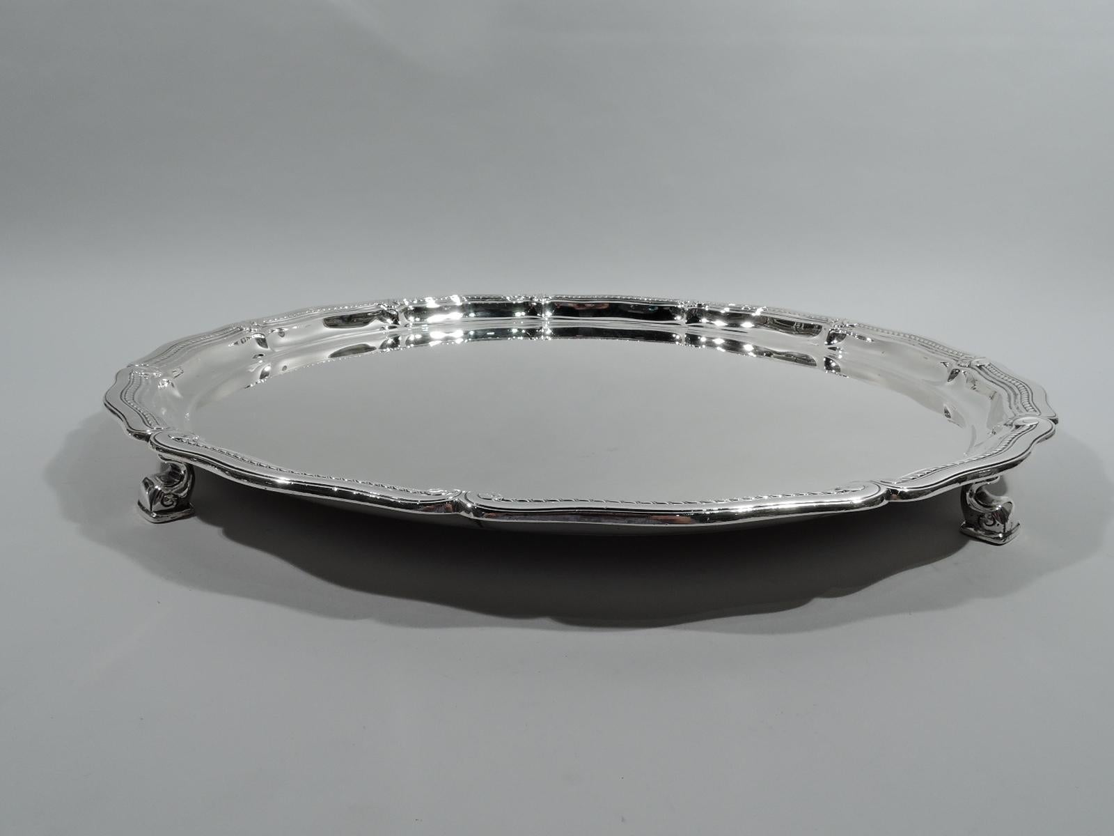 Edwardian Classical sterling silver tray. Made by Tiffany & Co. in New York, ca 1925. Round well. Rim has long and gently scrolls inset with rope border and Classical volute terminals interspersed with scallop shells. Four dolphin-style volute