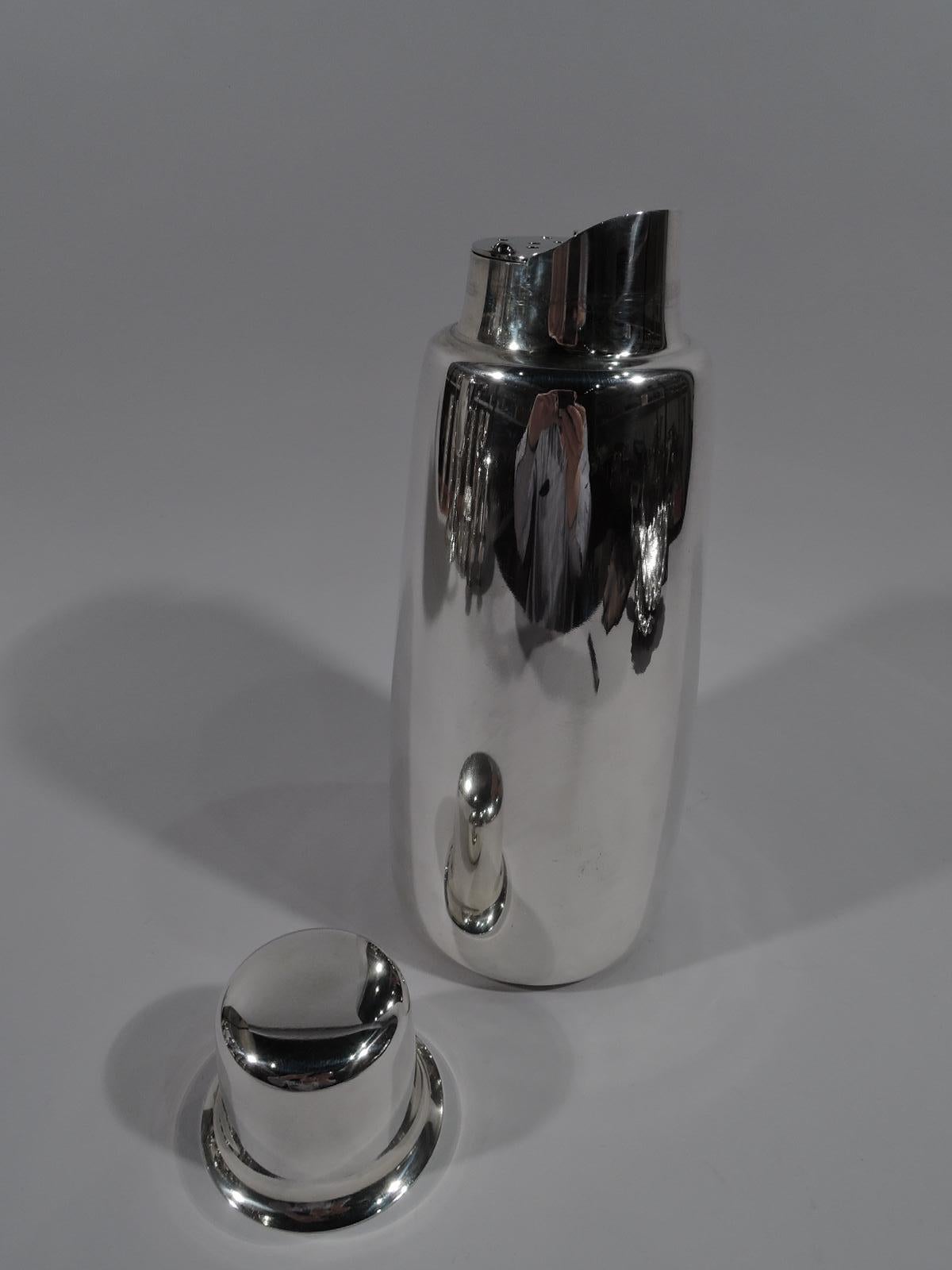 Mid-Century Modern sterling silver cocktail shaker. Made by Tiffany & Co. in New York. Upward tapering sides, short and inset neck with arched rim spout, and side-hinged pierced strainer. Jigger cover has flared rim. Gilt interior. Sleek and