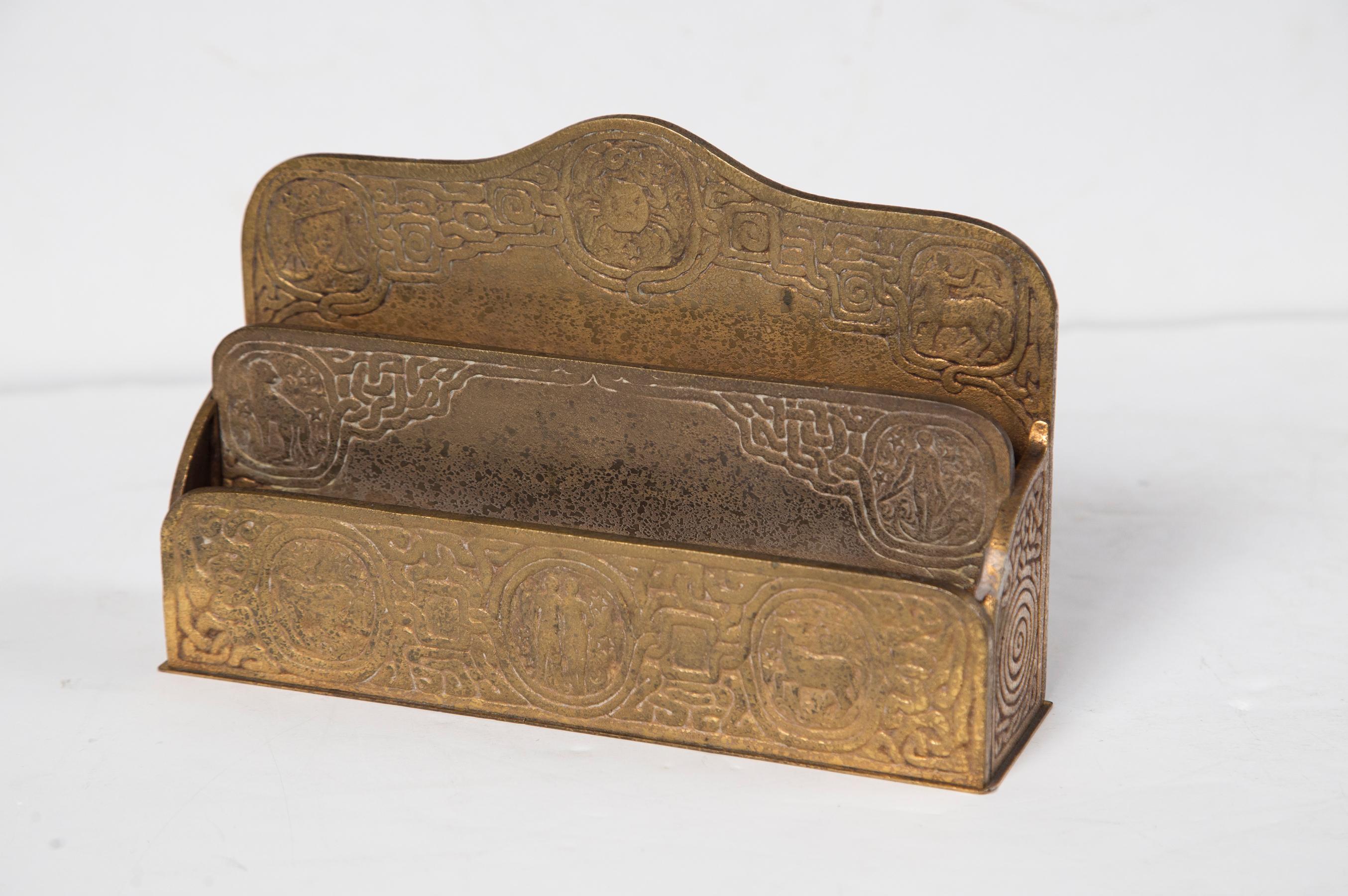 This letter holder in gilt bronze is in the Zodiac pattern. 
2 Compartments.
Stamped on the bottom TIFFANY STUDIOS, NEW YORK, 1009
.Please note that  all purchases  must  be completed  by  May 31, 2022  and collected  by June 29
