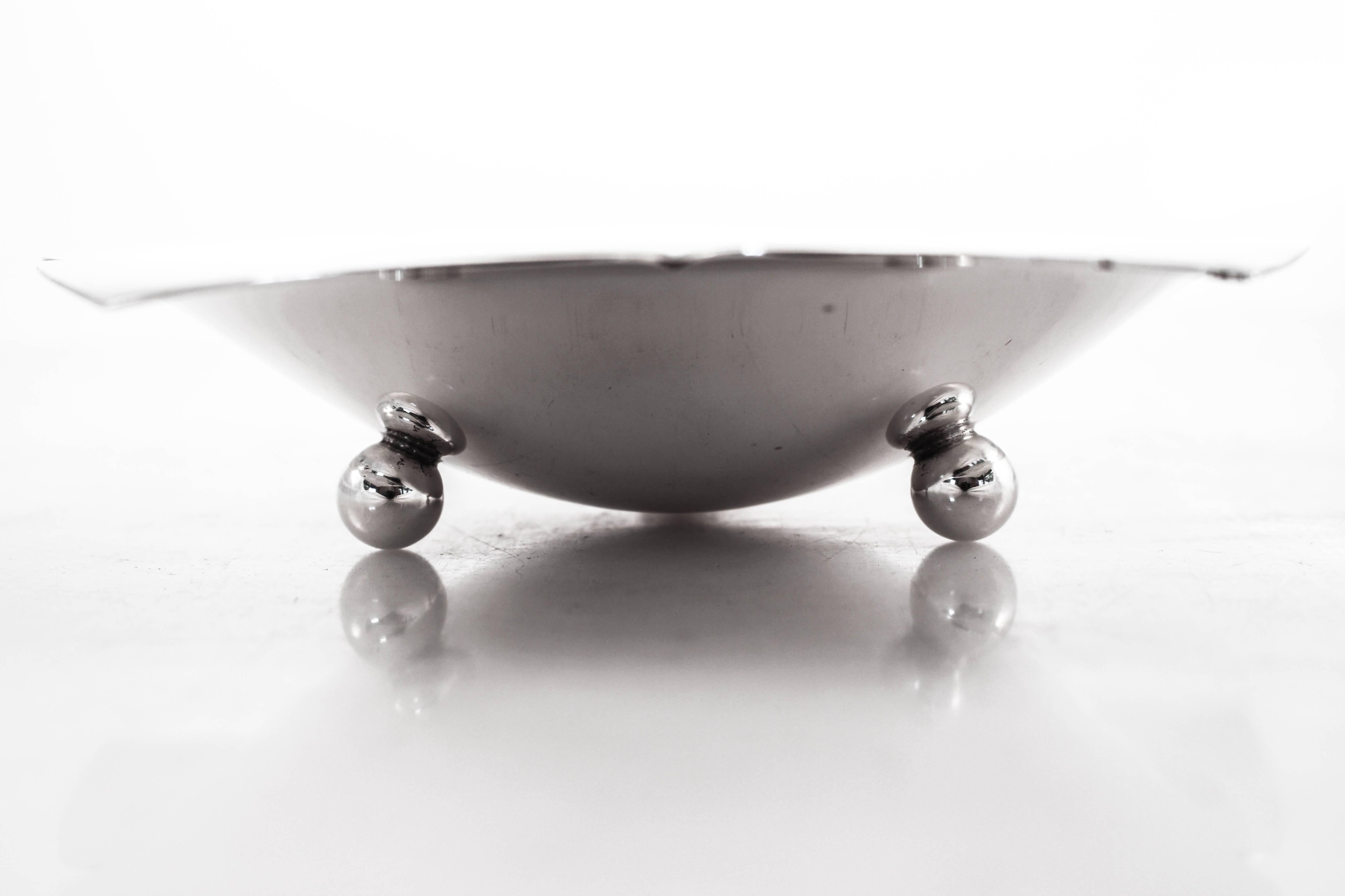 Like a flower blossoming, this Tiffany dish has the same shape; scalloped with five leaf-like pedals. It stands on three round - ball feet, raising it off the surface. The centre dips in, making it ideal for nuts or other small treats.
 