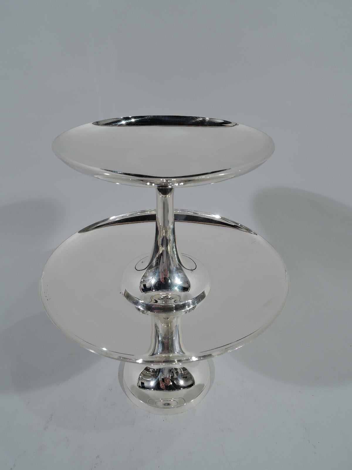 Rare Mid-Century Modern sterling silver two-tiered cake stand comprising two stacking compotes. Made by Tiffany & Co. in New York. Each compote has a raised foot, upward tapering stem, and shallow disc bowl. The small compote’s foot fits on the