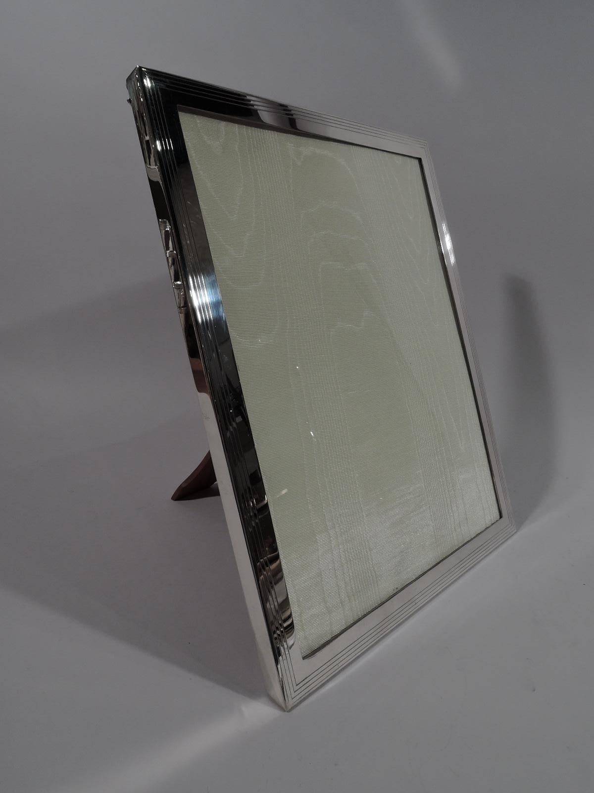 Mid-Century Modern sterling silver picture frame. Made by Tiffany & Co. in New York. Rectangular window and flat surround with three engraved wraparound lines. With glass, silk lining, and stained-wood back and support. For portrait (vertical)