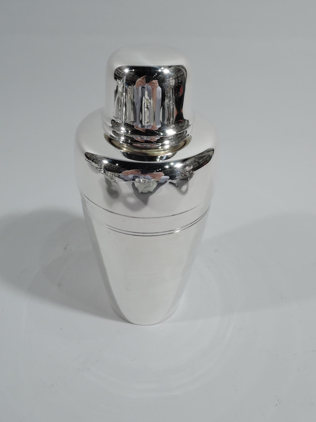 Mid-Century Modern sterling silver cocktail shaker. Made by Tiffany & Co. in New York. The classic bullet form with tapering cup, curved shoulders, and inset spout with built-in strainer. Cap has flared rim. Spare with incised bands. Nice pint size