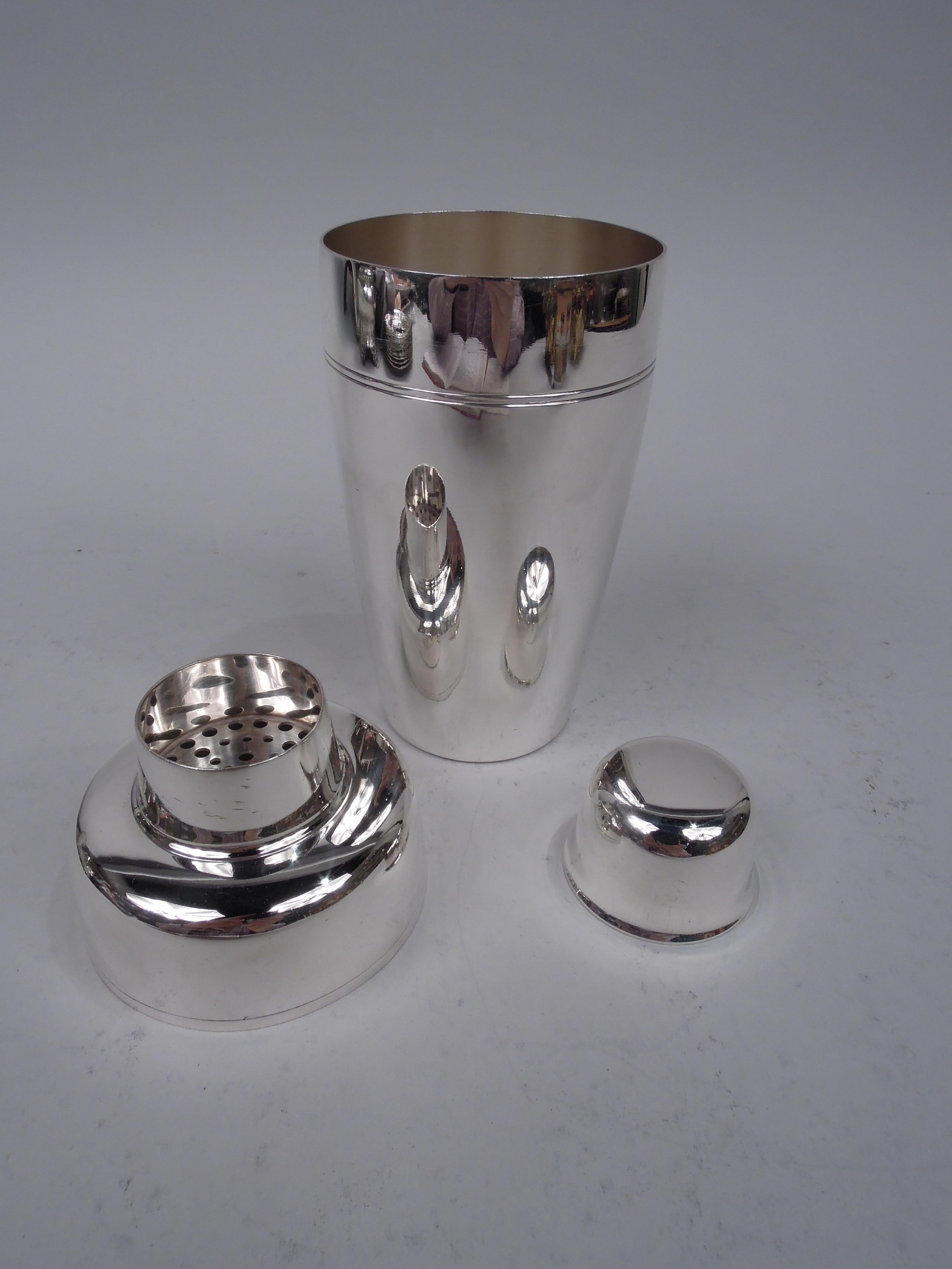 Midcentury Modern sterling silver cocktail shaker. Made by Tiffany & Co. in New York. The classic bullet form with tapering cup, curved shoulders, and inset spout with built-in strainer and snug-fitting jigger cap. Spare with incised bands. Nice