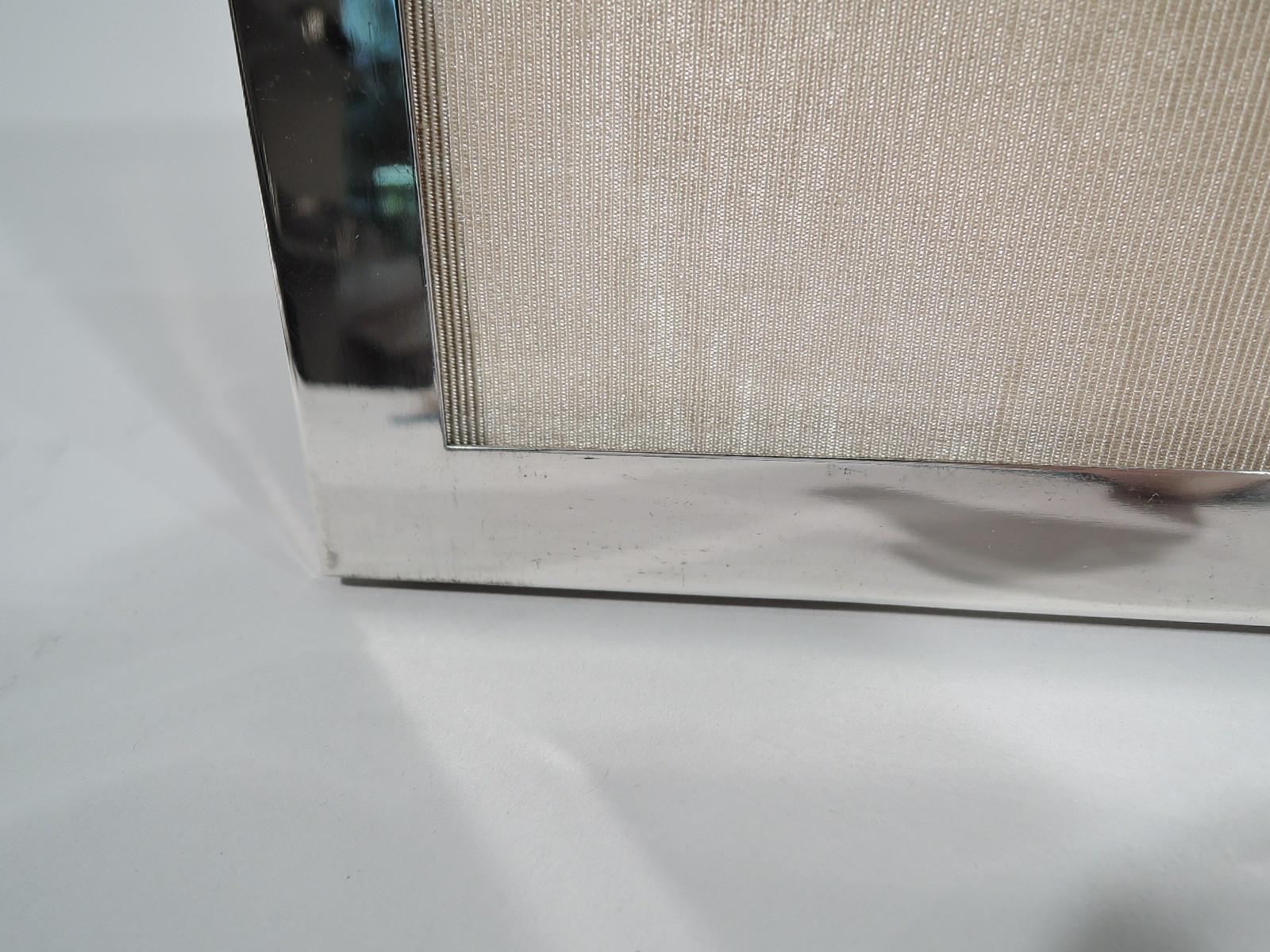 Modern sterling silver frame. Retailed by Tiffany & Co. In New York. Rectangular window in plain and flat surround. With glass, silk lining, and velvet back and hinged easel support for portrait (vertical) or landscape (horizontal) display. Marked