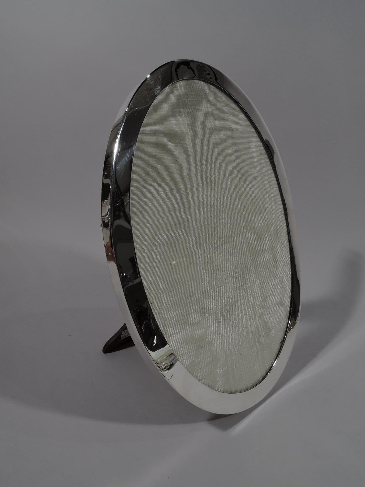 Modern sterling silver picture frame. Made by Tiffany & Co. in New York, circa 1910. Oval window with flat surround. With glass, silk lining, and stained-wood back and hinged support. Fully marked including pattern no. 16101 and director’s letter