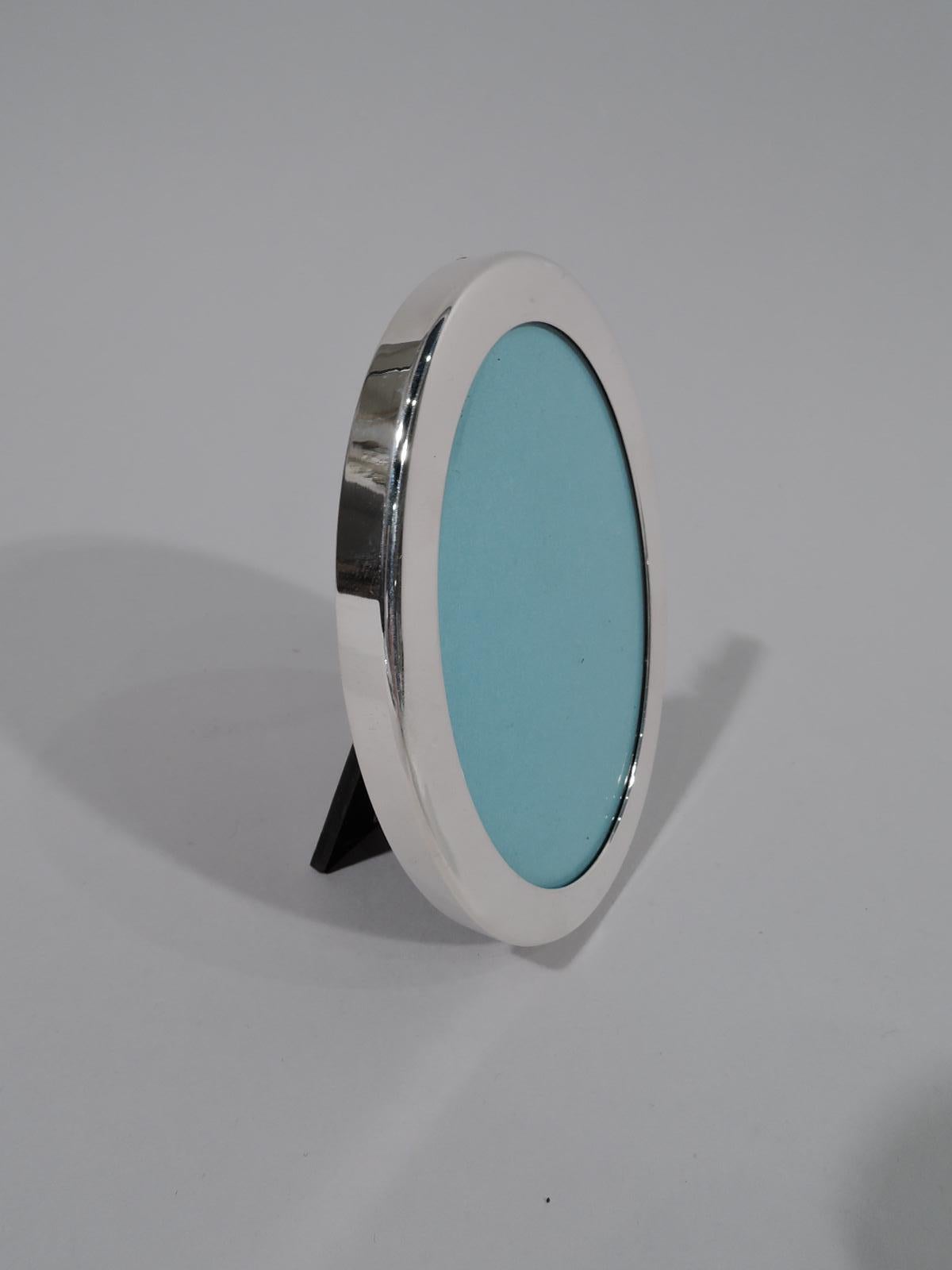 Small sterling silver picture frame. Retailed by Tiffany & Co. in New York. Oval window and flat surround. With glass, eggshell-blue lining, and laminate back and hinged support. Marked “Tiffany & Co. / Sterling” and post-1967 Italian hallmark for