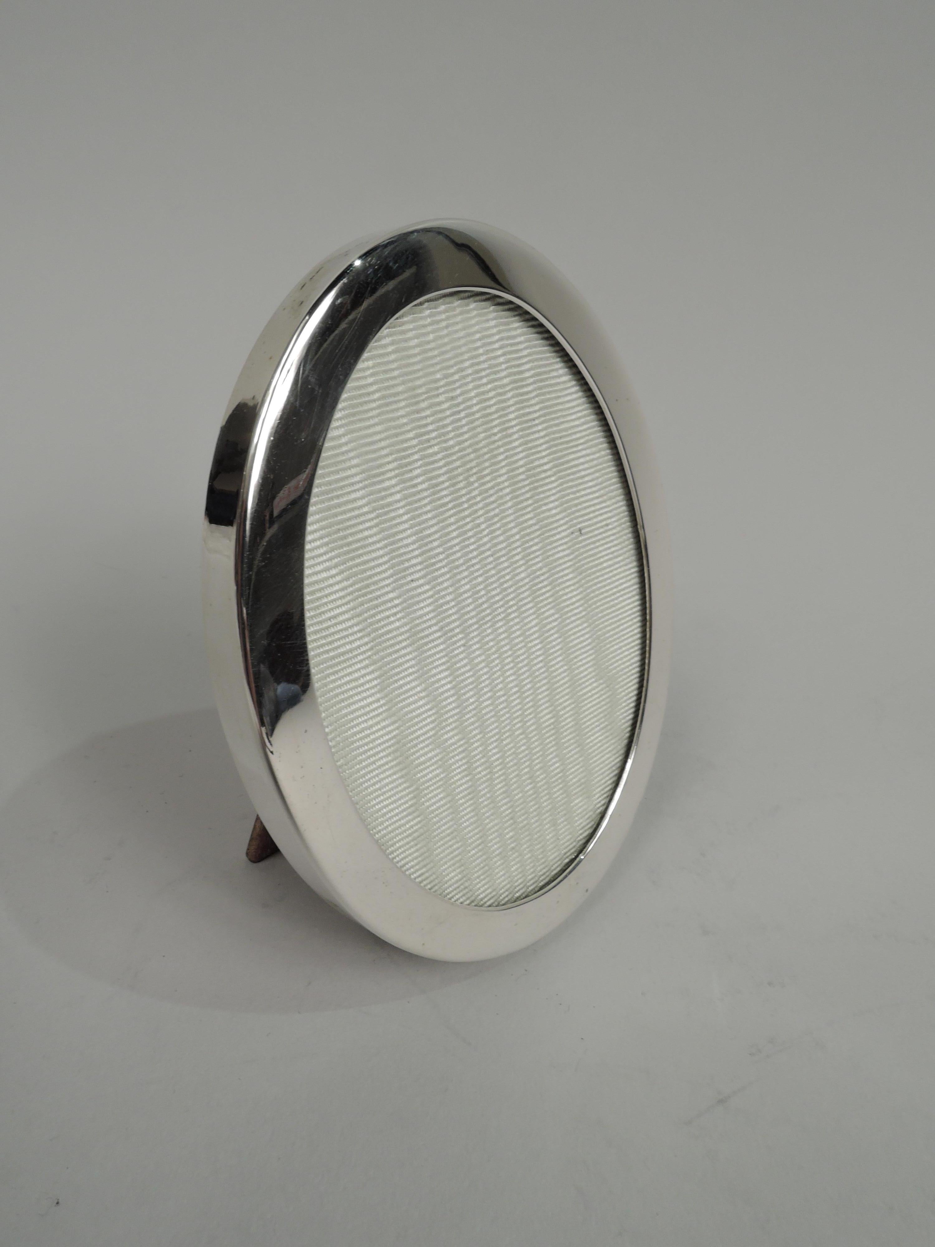 Small sterling silver picture frame. Made by Tiffany & Co. in New York. Oval window and flat surround. With glass, liner, and wood back and hinged easel support. Marked “Tiffany & Co. Makers Sterling”. 

Dimensions: Frame: H 3 3/4 x W 3 in.