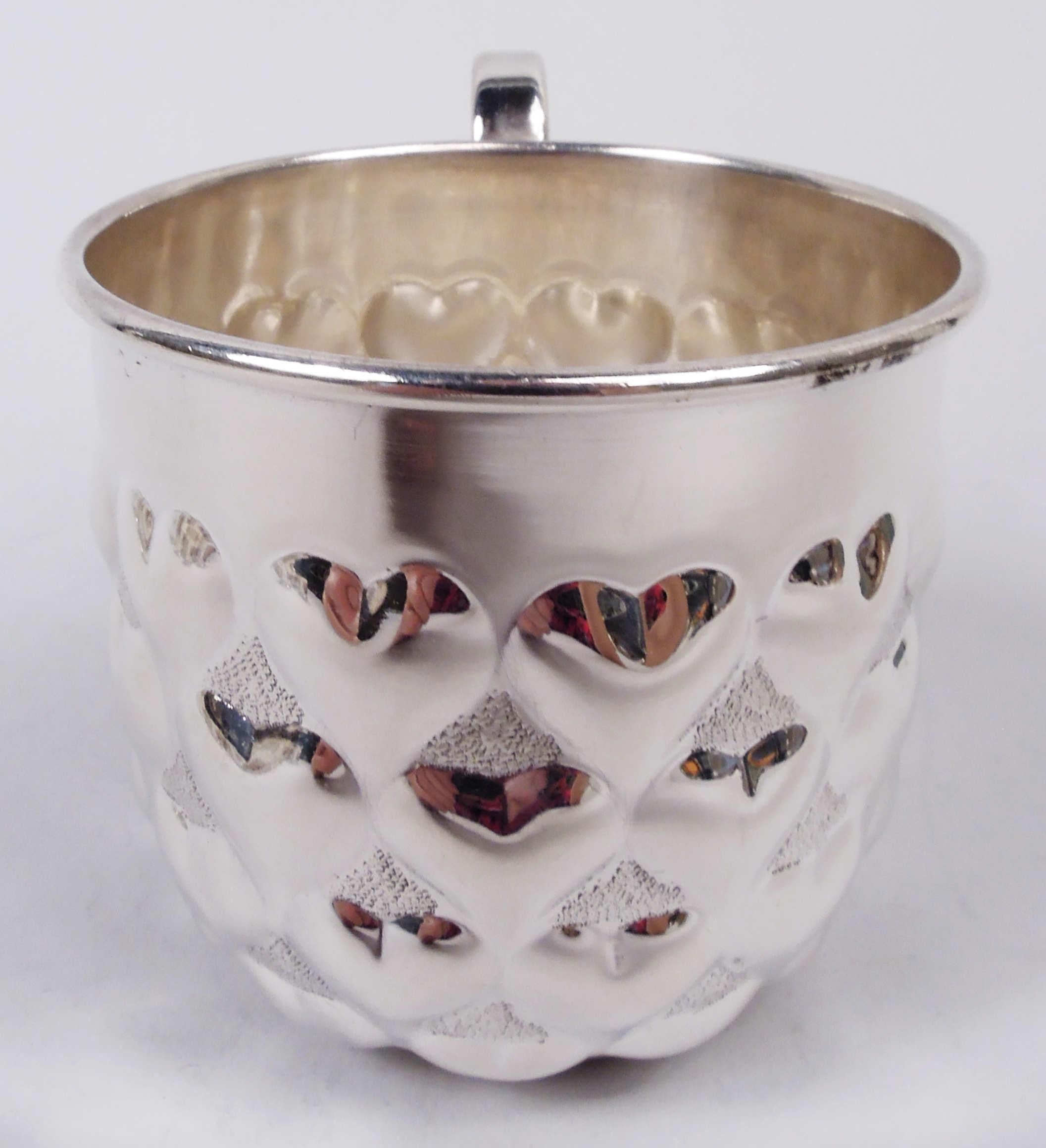 Modern sterling silver baby cup. Retailed by Tiffany & Co. In New York. Gently curved sides with rows of embossed hearts on stippled ground. Top vacant. High-looping scroll handle. Marked “Tiffany & Co. / Sterling / Italy” with post-1967 Italian