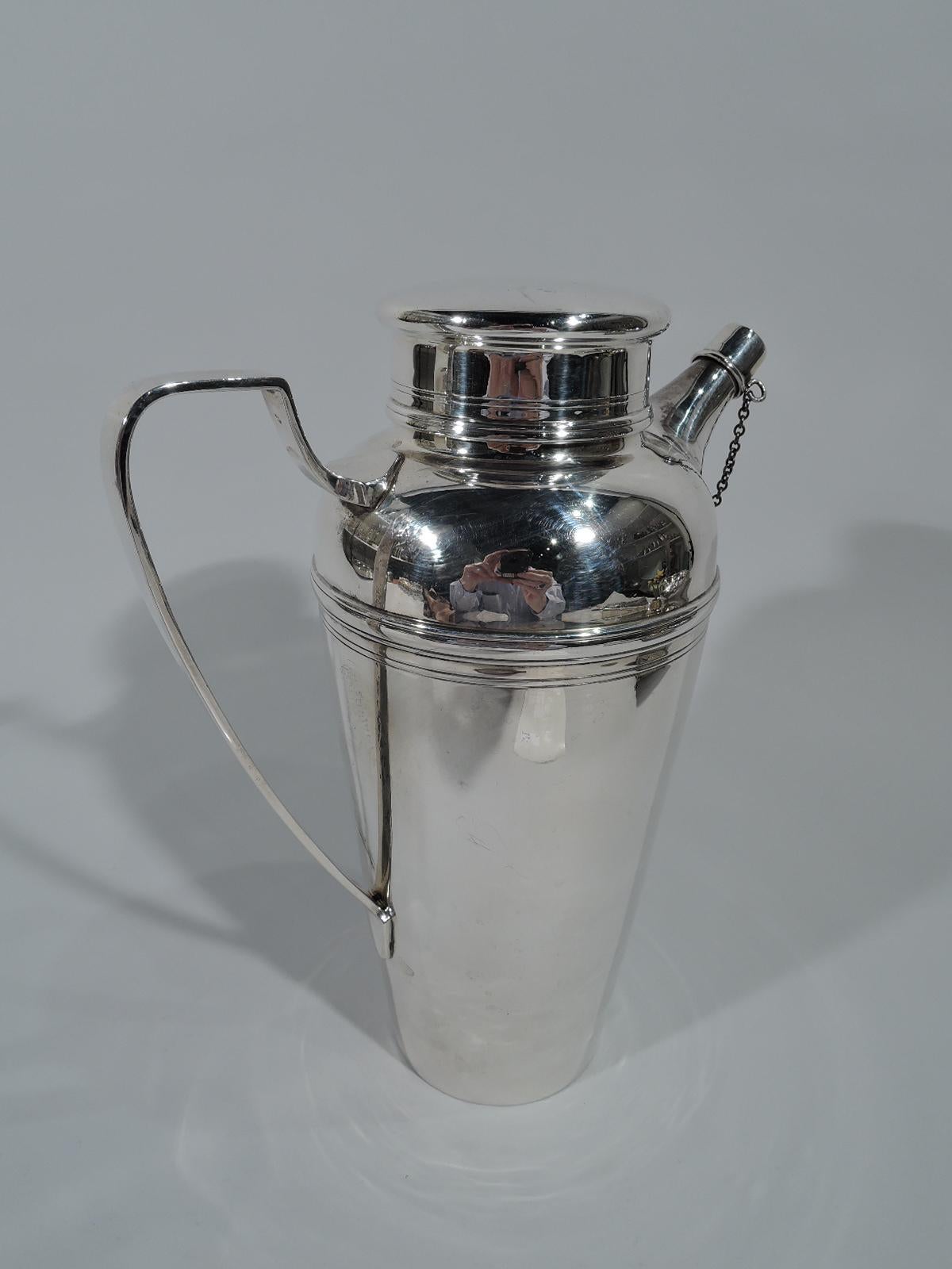 Modern sterling silver cocktail shaker. Made by Tiffany & Co. in New York, circa 1925. Tapering sides, short neck, flat and overhanging cover, scroll bracket handle, and diagonal spout with built-in strainer and chained cap. Spare with incised