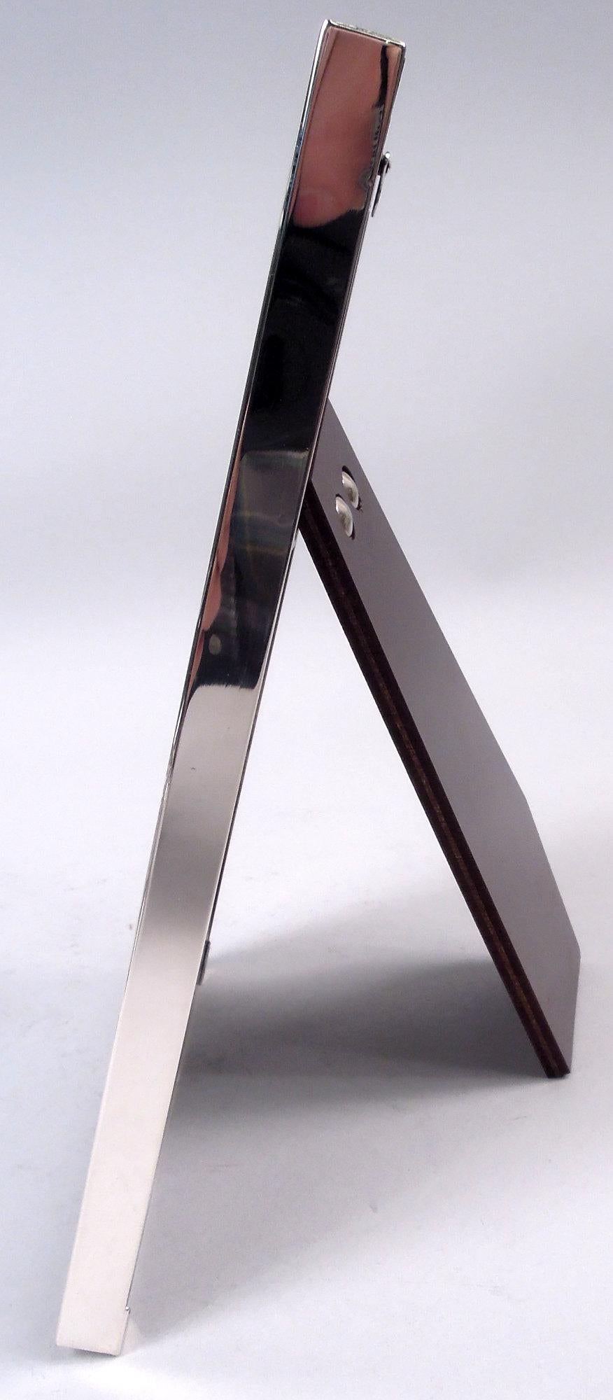 Modern sterling silver picture frame. Rectangular window in wide and flat surround. Applied to upper-left corner is silver and enamel figure of Jack springing out of the box. With glass, eggshell blue paper lining, and wood laminate back and hinged