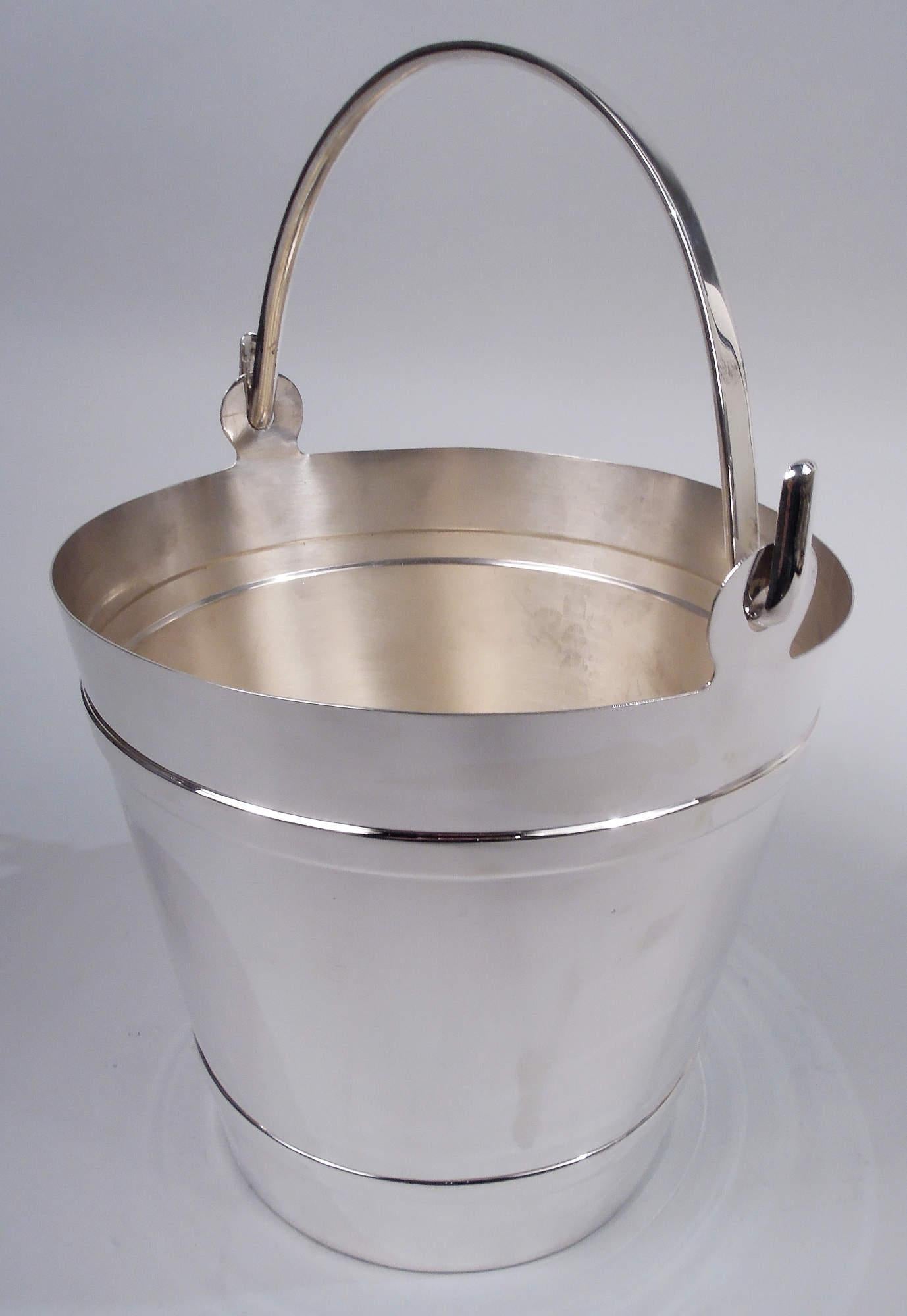 Modern sterling silver ice bucket. Retailed by Tiffany & Co. in New York. Straight and tapering sides with embossed hoops and flat c-scroll swing handle. Post-1967 Italian marks including maker’s stamp for Ganci Argenterie and retailer’s stamp.