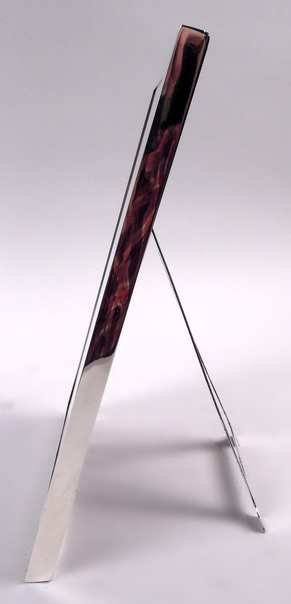 Modern sterling silver picture frame. Made by Tiffany & Co. in New York, ca 1910. Rectangular window in flat and plain surround. With glass, silk lining, stained-wood back, and hinged easel silver support. Fully marked including maker’s stamp,