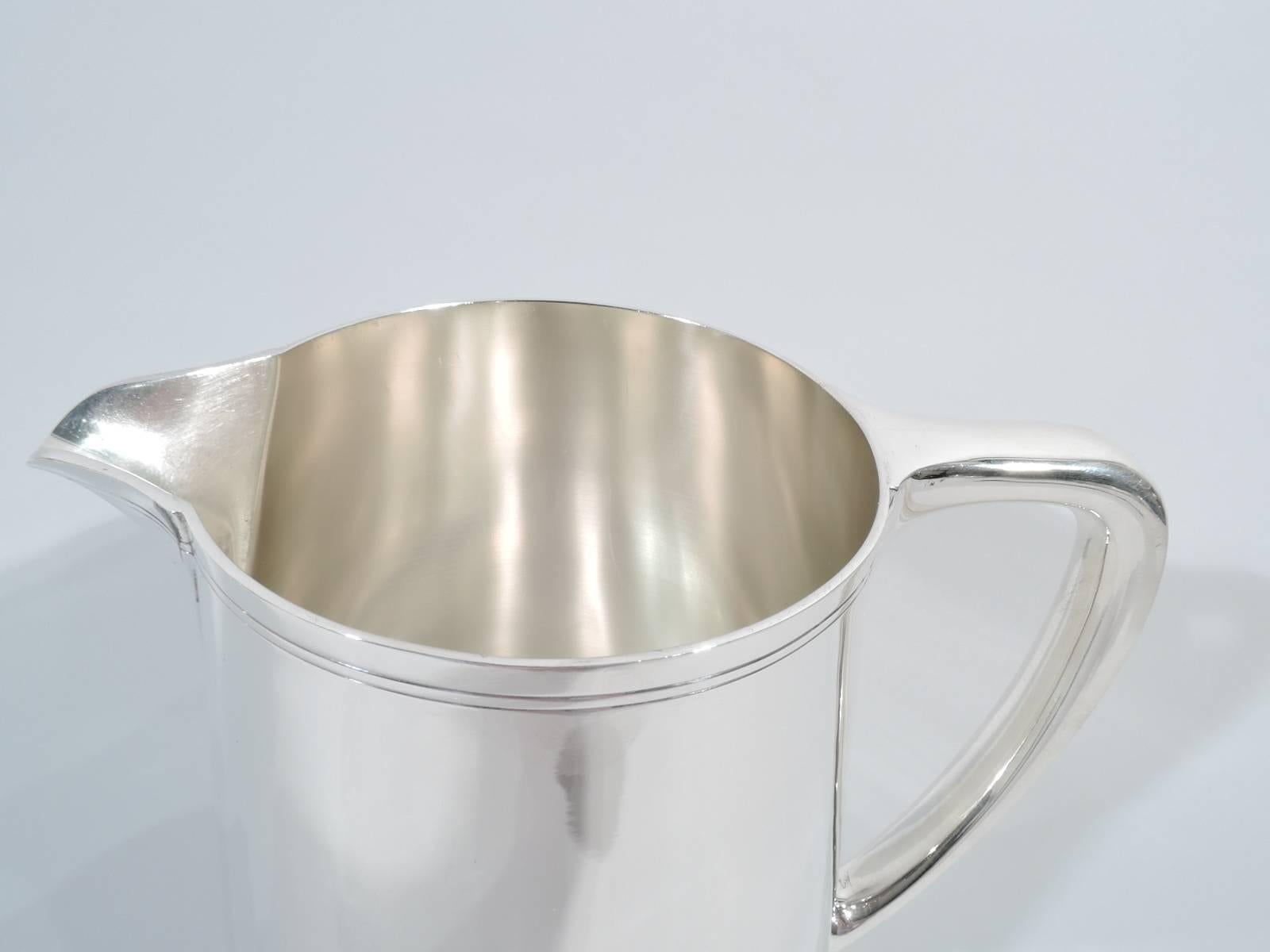 Sterling silver water pitcher. Made by Tiffany & Co. in New York. Upward tapering sides, scrolled bracket handle, and V-spout. Softened Modernism with spare incised banding around rim and spout. Hallmark includes pattern no. 22343 and director's