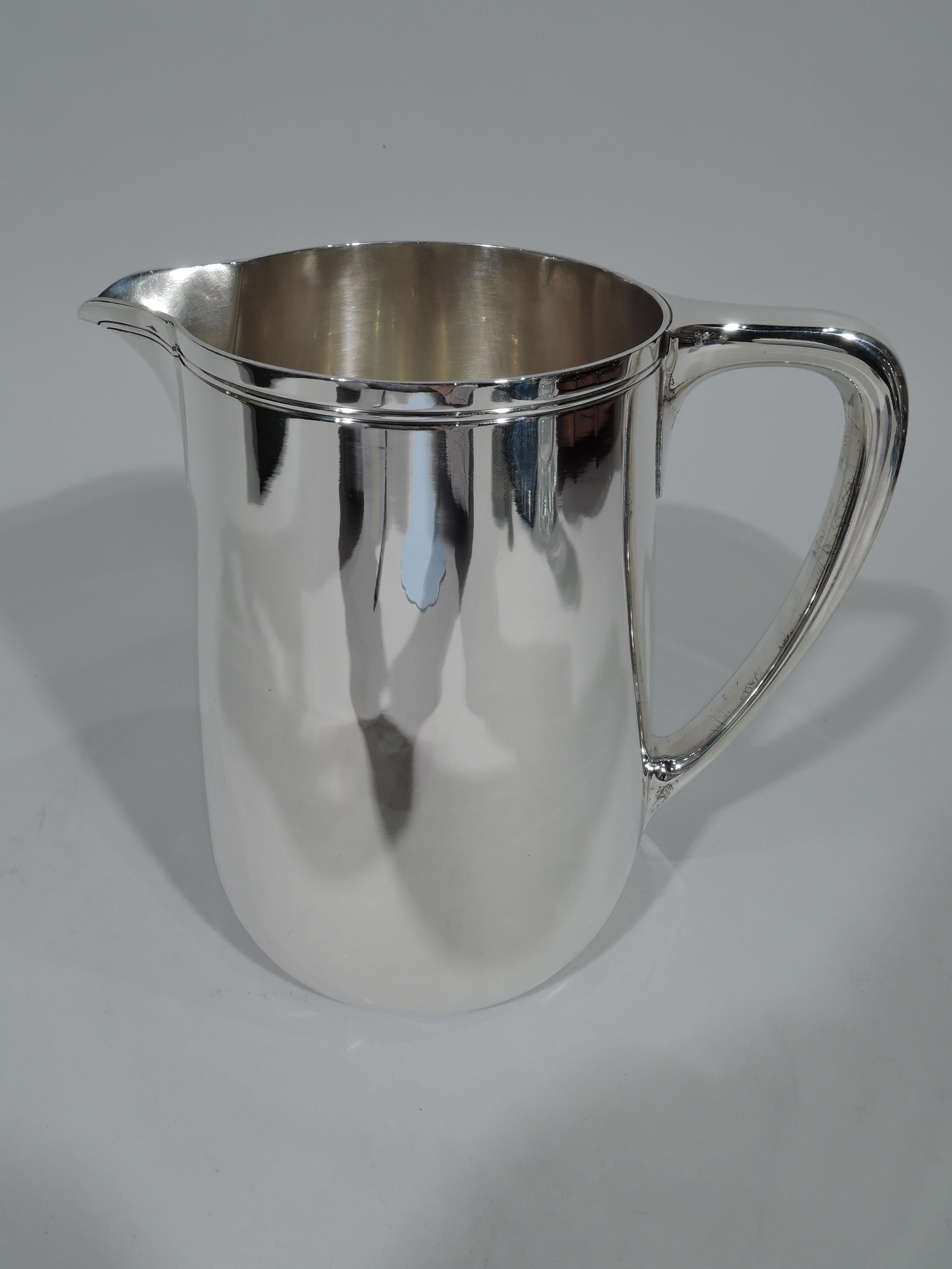 Modern sterling silver water pitcher. Made by Tiffany & Co. in New York. Upward tapering sides, scrolled bracket handle, and v-spout. Spare incised banding near rim. Holds 3 1/2 pints. Hallmark includes pattern no. 22343, director's letter m