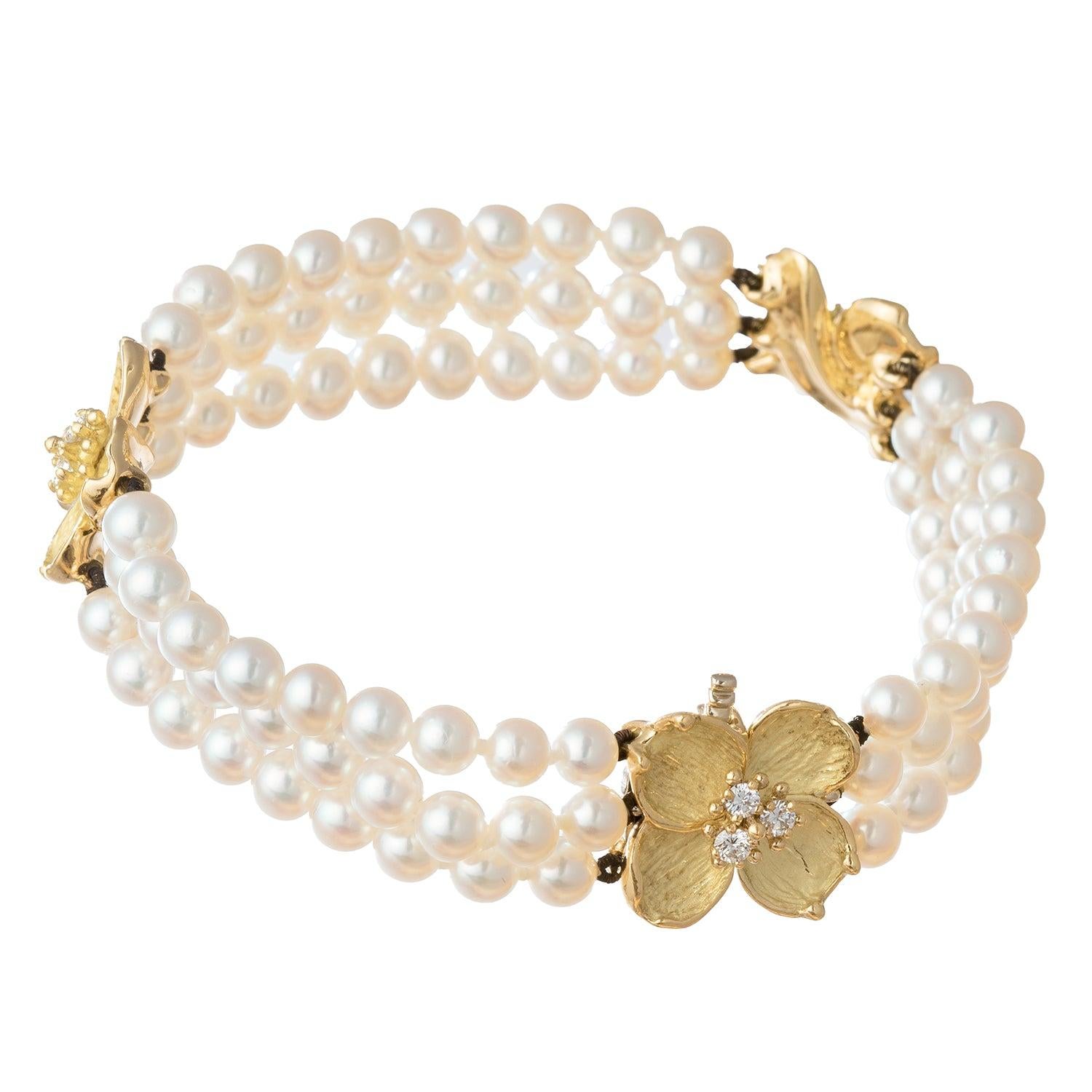 Tiffany & Co. three-strand cultured pearl bracelet separated by two dogwood flower blossom motifs in 18 karat yellow gold with satin textured petals and brilliant-cut diamond-set pistils at center. Nine diamonds weighing approximately 0.36 total