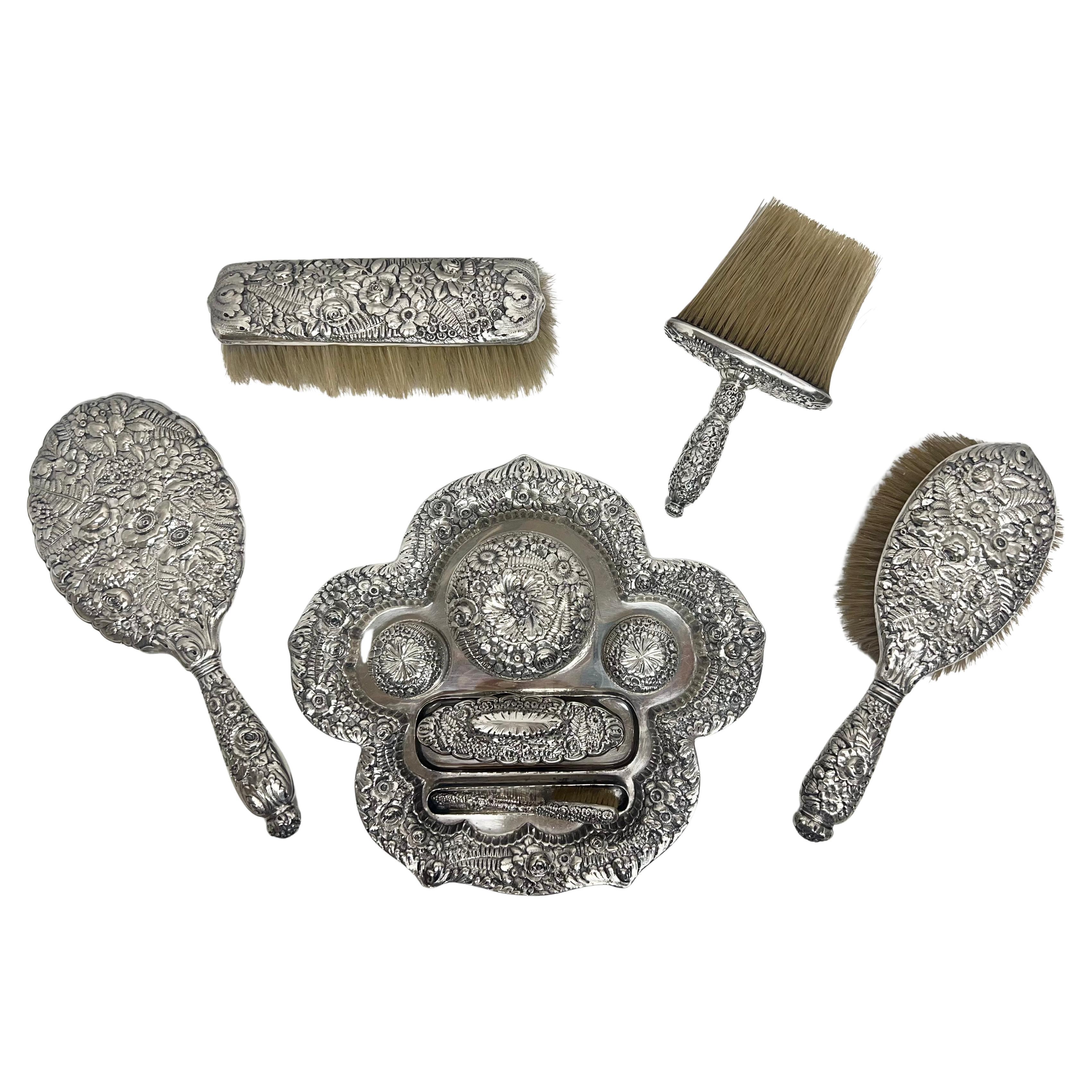 Tiffany & Co. sterling silver eleven-piece vanity dresser set in Tiffany's iconic repoussé flower and leaf pattern, circa 1890.  Includes tray, larger circular covered dish, two small pill size covered boxes, small demi-brush, nail buffer, mirror,