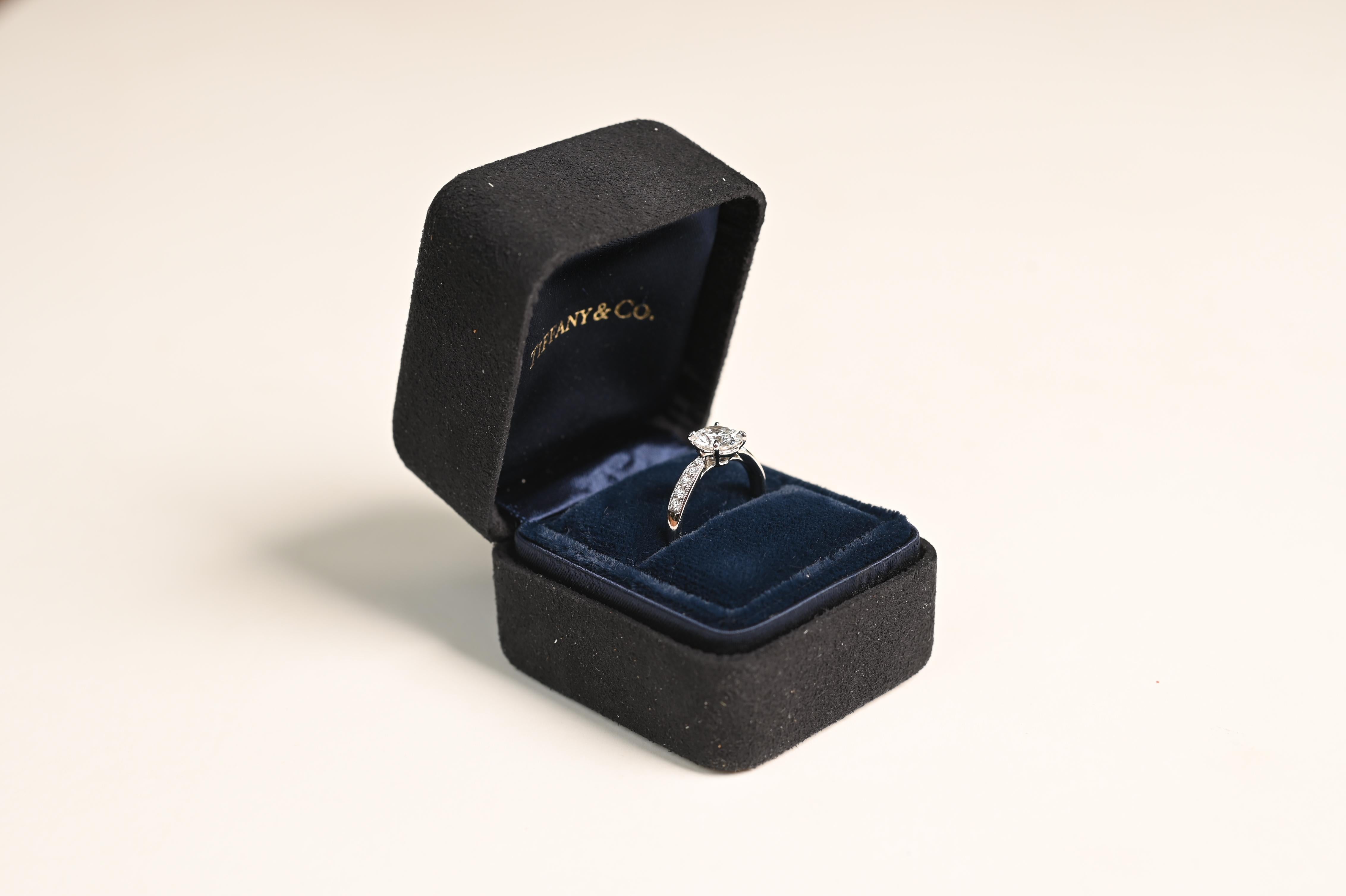 This exquisite platinum engagement ring from Tiffany & Co. is a timeless piece of fine jewelry, featuring a GIA-certified round brilliant cut diamond as its centerpiece. Weighing an impressive Approx. 1.1-Carats, the diamond exhibits a dazzling G
