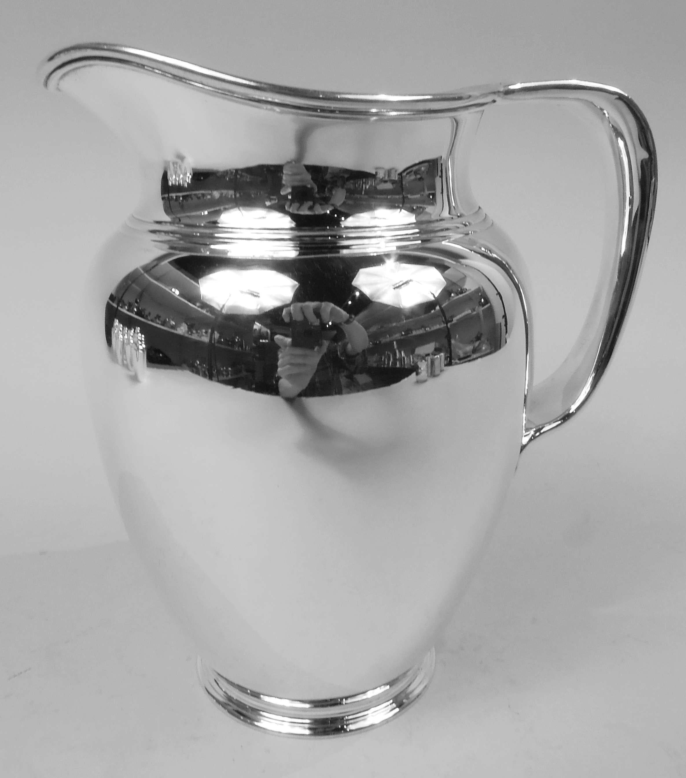 Modern sterling silver water pitcher. Made by Tiffany & Co. in New York, ca 1907. Ovoid body, stepped foot, short neck, and helmet mouth; soft bracket handle with trefoil shaped tail mount. A spare full-bodied vessel. Nice heft. Fully marked