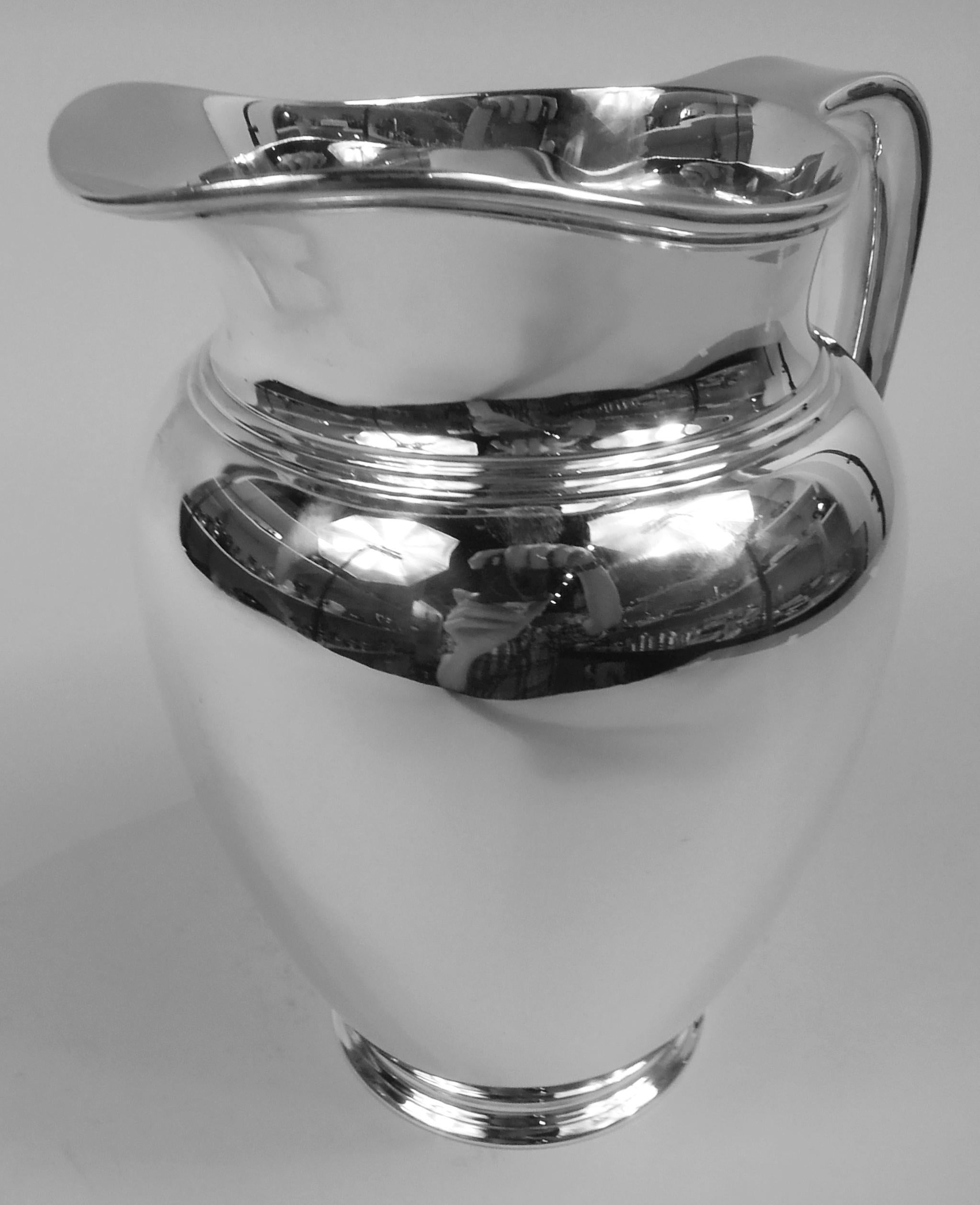 Modern sterling silver water pitcher. Made by Tiffany & Co. in New York, ca 1907. Ovoid body, stepped foot, short neck, and helmet mouth; soft bracket handle with trefoil shaped tail mount. A spare full-bodied vessel. Nice heft. Fully marked
