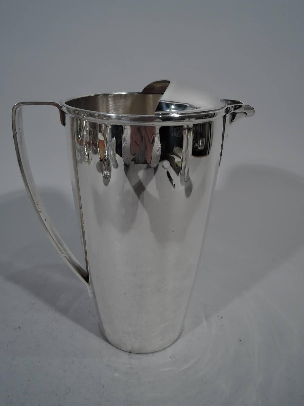 Classic Midcentury Modern sterling silver bar pitcher. Gently curved and tapering sides, scrolled bracket handle, and soft u-spout with built-in strainer. Open top with demi-lune ice guard. Hallmark includes pattern no. 23058 and director’s letter M