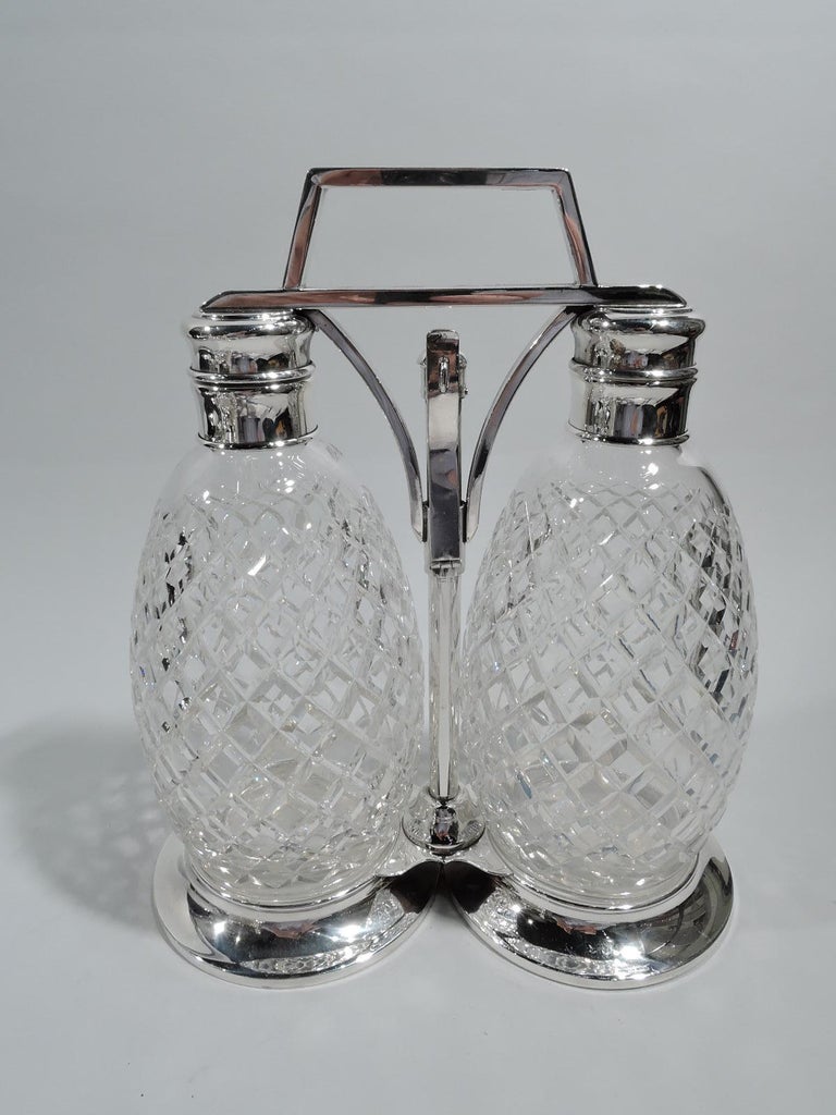 Mid-Century Modern sterling silver decanter set. Retailed by Tiffany & Co. in New York. Sterling silver frame with central pole on shaped base between two round and open wells. Pole has sliding mechanism with hinged hasp and bracket handle to which