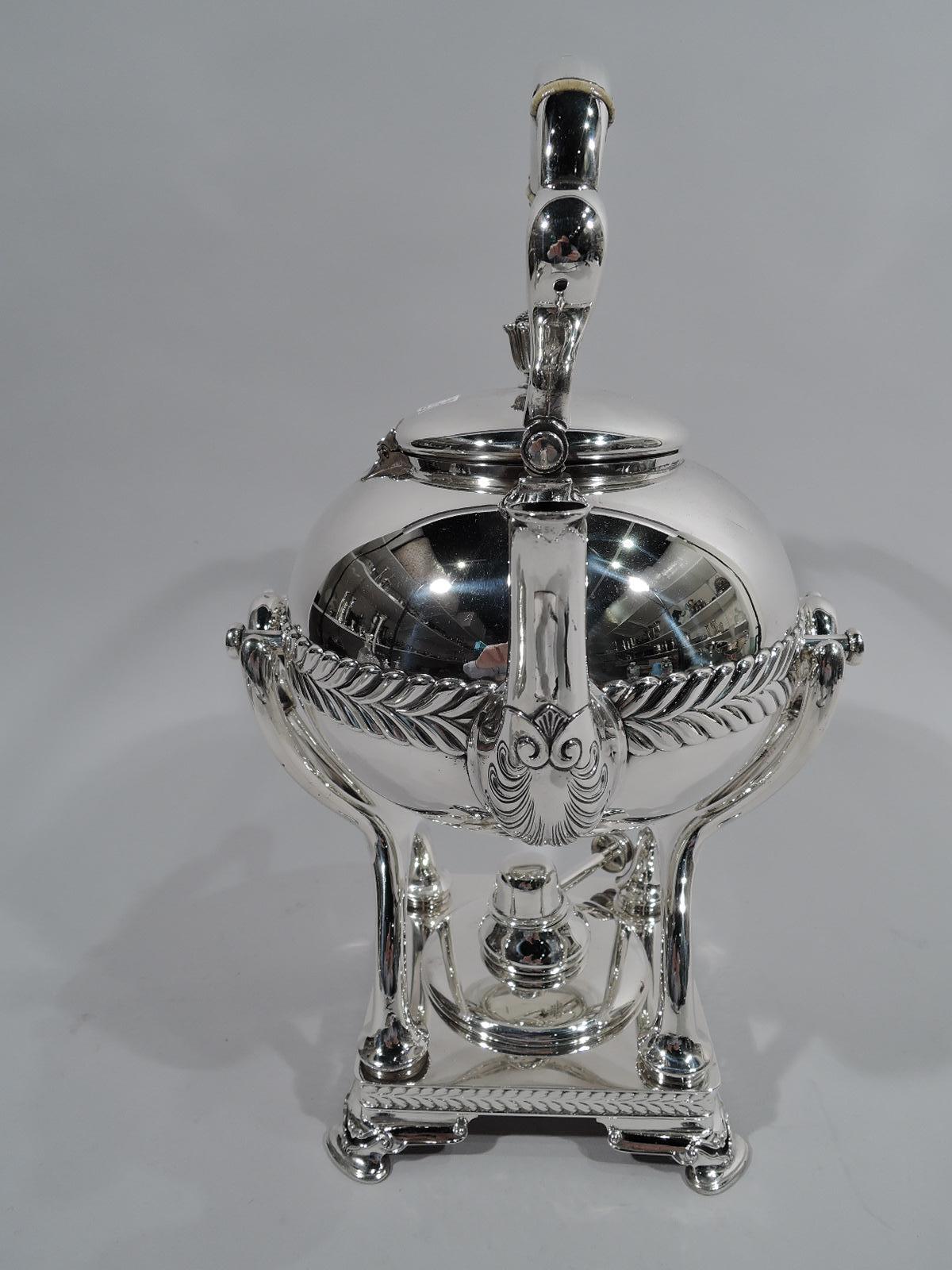 Stylish sterling silver hot water kettle on stand. Made by Tiffany & Co. in New York, circa 1910. Kettle: Globular with upright spout, swing trefoil handle, and side-hinged cover with stylized bud finial. Stand: Square with open heraldic shield