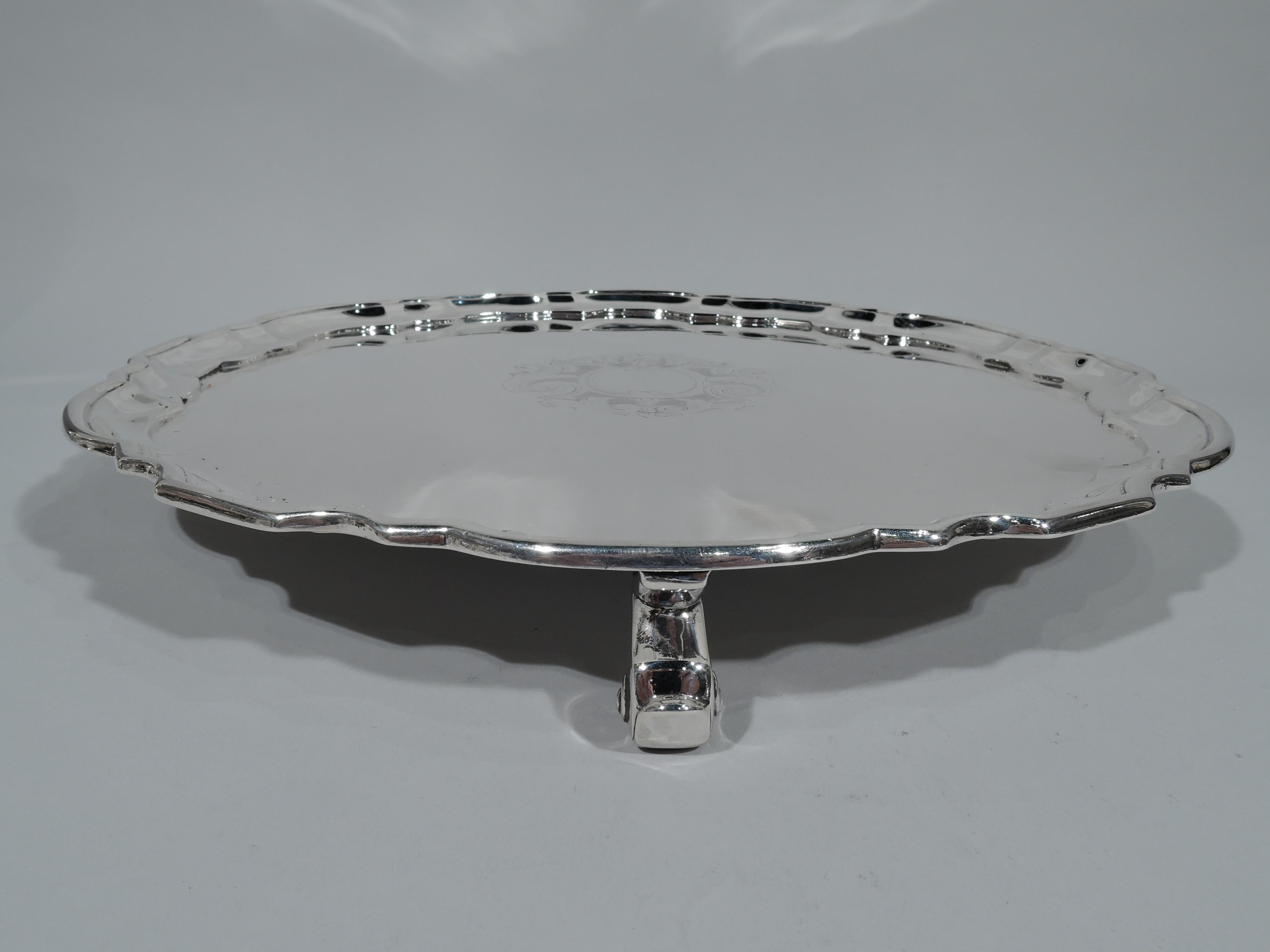 Traditional sterling silver salver. Made by Tiffany & Co. in New York, circa 1931. Circular with molded curvilinear piecrust rim. Scrolled frame (vacant) with fancy leaf-and-scroll surround engraved in well center. Rests on 4 capped volute scroll
