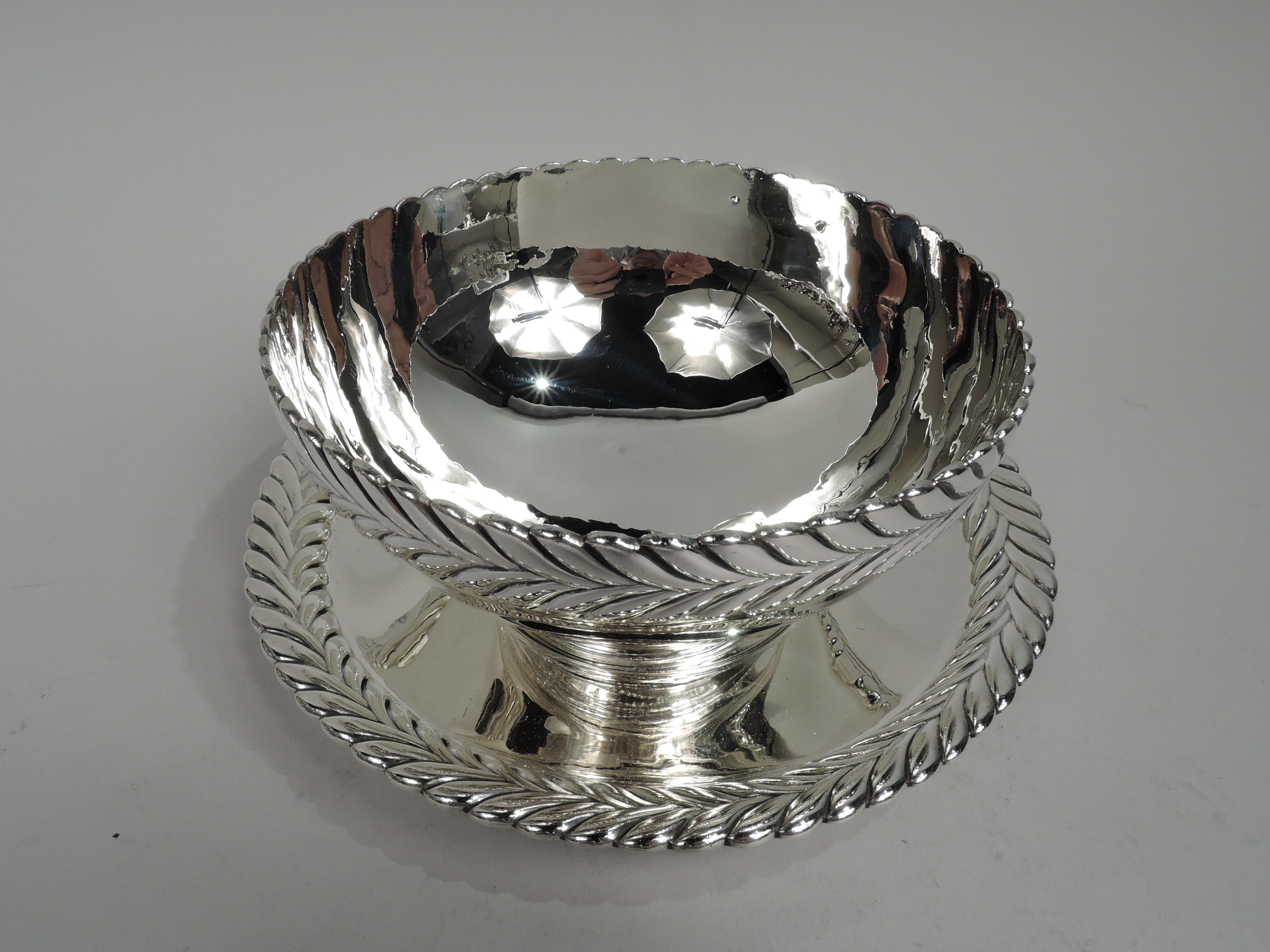 Stylish sterling silver sauce bowl on stand. Made by Tiffany & Co. in New York. Bowl: Curved sides and stepped foot. Stand: Round well and gently curved sides. Rims have applied border in form of bold imbricated leaves or chevrons. A popular motif