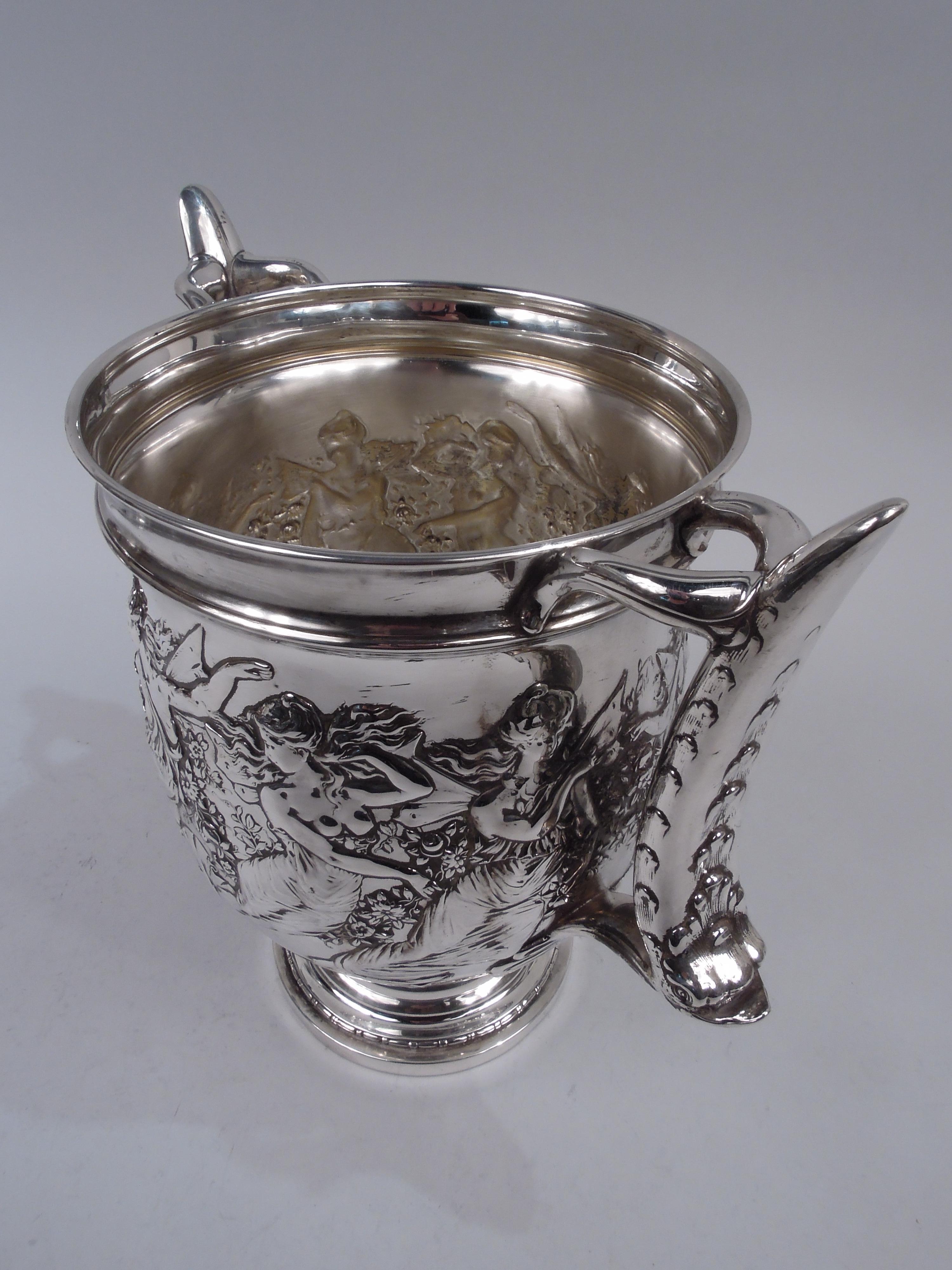 Victorian sterling silver wine cooler. Deep ovoid bowl on raised foot. Leaf-capped dolphin scroll-bracket side handles. Bead-and-reel and leaf-and-dart borders. Chased frieze depicting garland-entwined, barefooted, long-tressed nymphs, their loose