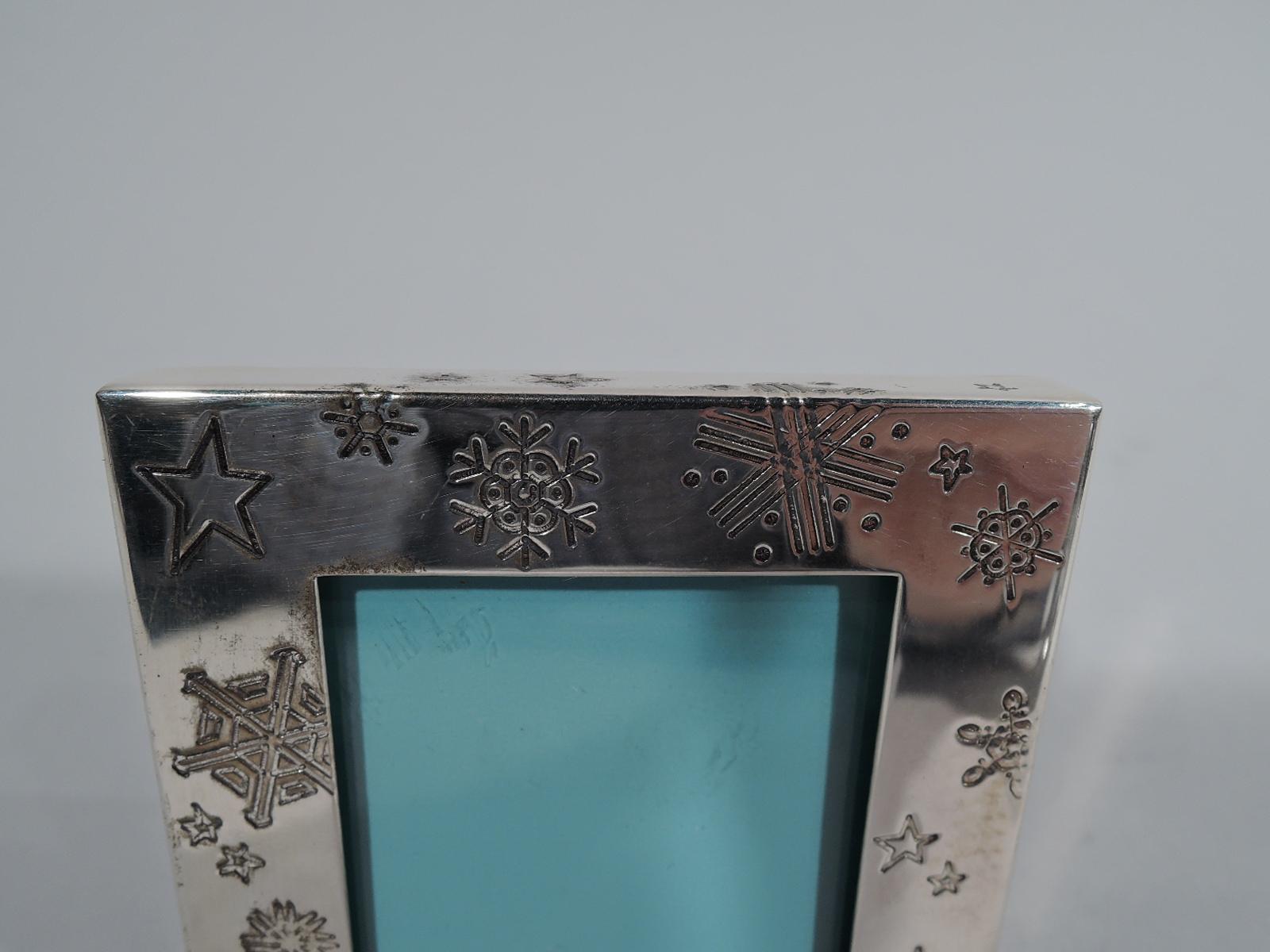 Winter wonderland sterling silver picture frame. Retailed by Tiffany & Co. in New York. Square window in flat surround with engraved (meteorological) snowflakes scattered on front and sides. With glass, eggshell blue liner, and black laminate back