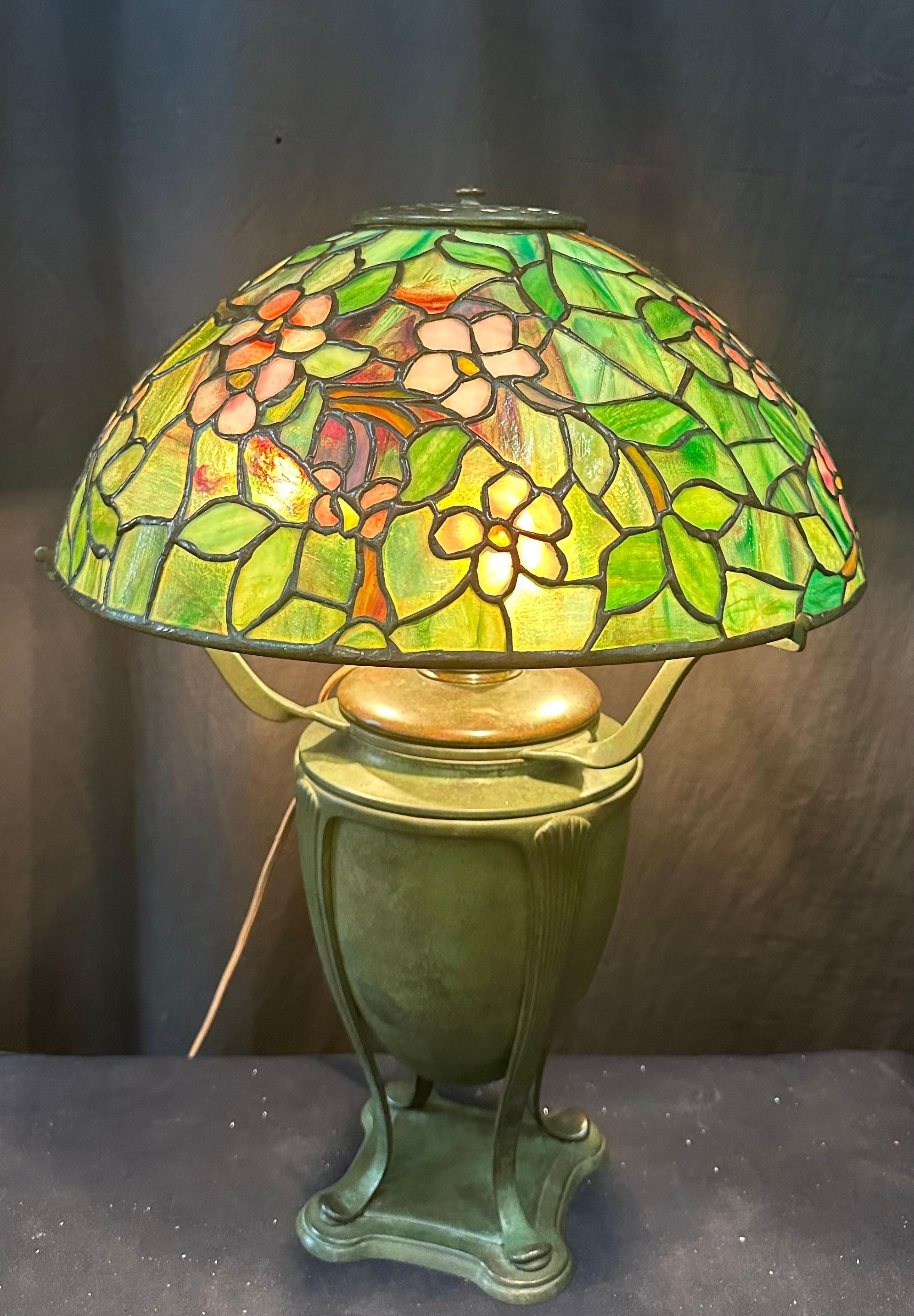 The Apple Blossom 16” diameter shade is signed “Tiffany Studios, New York” & numbered “1455”.The shade rests on a “Greek Urn” base with canister. The canister is signed “Tiffany Studios” and numbered “181”.The lamp is newly rewired & works