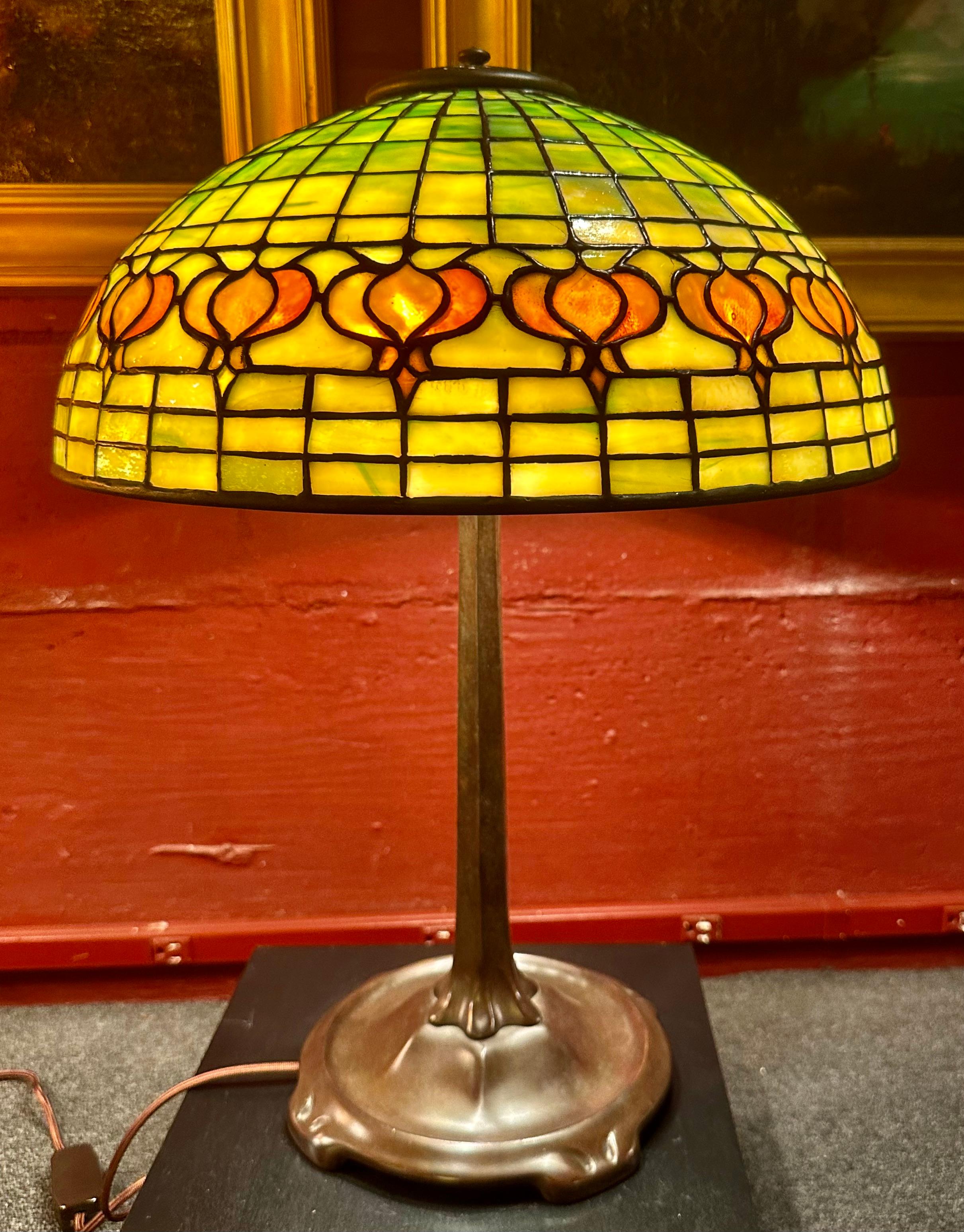 A Tiffany Studios orange geometric lampshade with a band of deeper orange  pomegranates circling the shade. This leaded lamp shade is signed “Tiffany Studios” with an early tag. It now rests on a patinated Tiffany Studios “stick” base. The lamp is