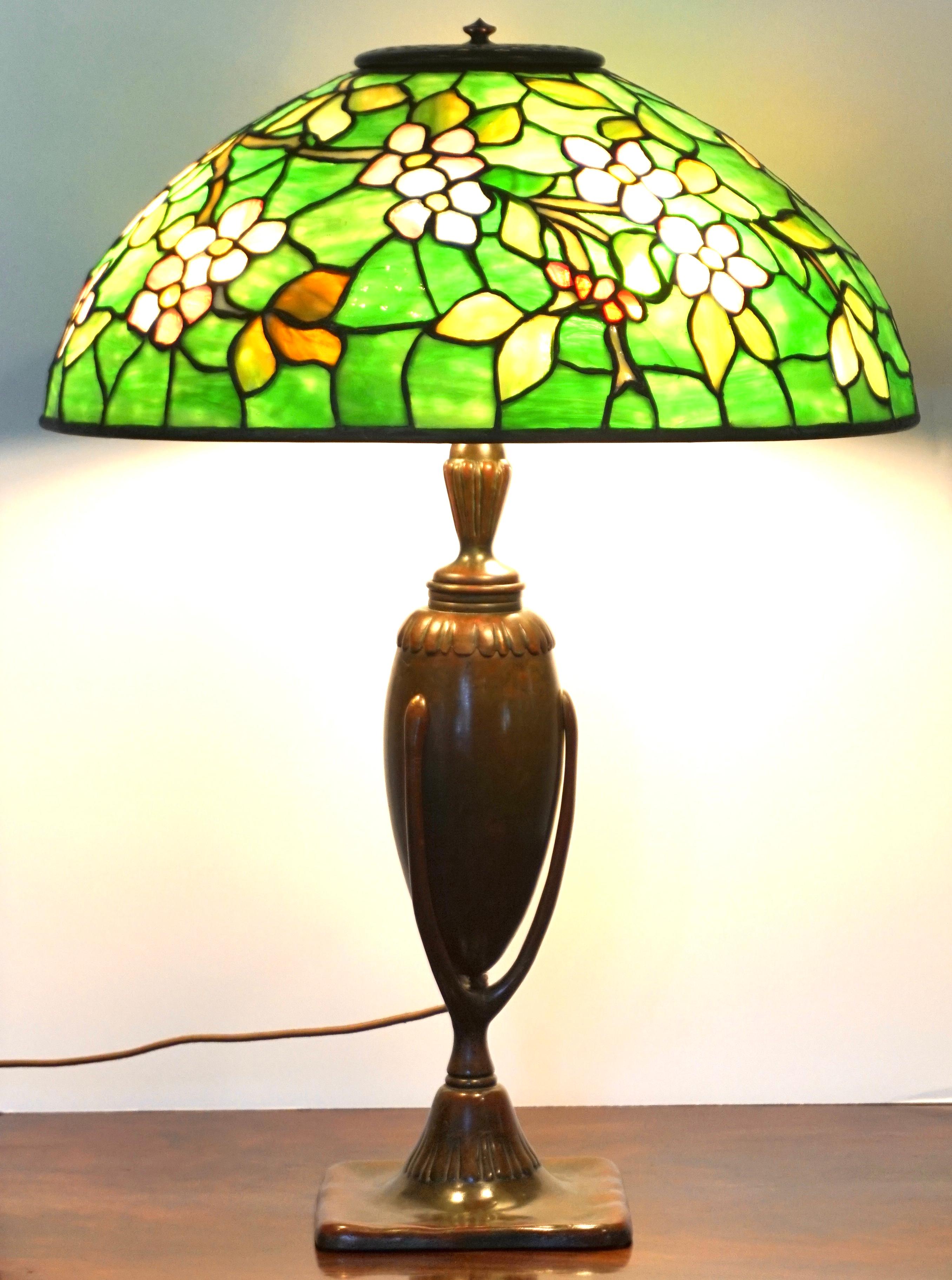 A fine Tiffany Favrile glass and bronze apple blossom table lamp, Tiffany Studios, New York, circa 1910 Art Nouveau. The domical leaded glass shade with an overall pattern of apple blossoms in pink and white striated opalescent glass, the leaves and