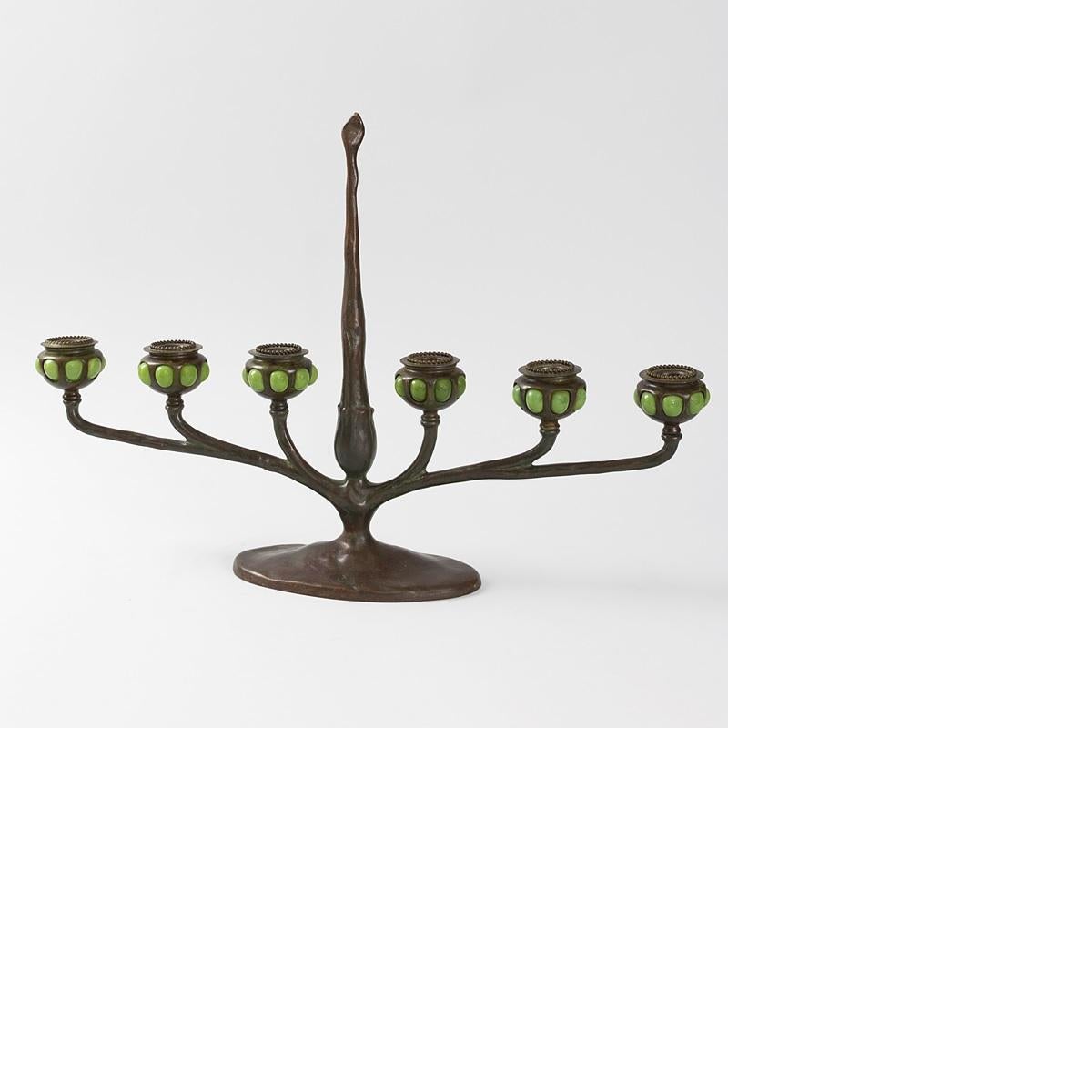 An American Art Nouveau patinated bronze and favrile glass mounted table candelabrum by Tiffany Studios New York. The candelabrum has six arms. Each candle holder is decorated with green favrile jewels. Circa 1910. A similar candelabrum is pictured