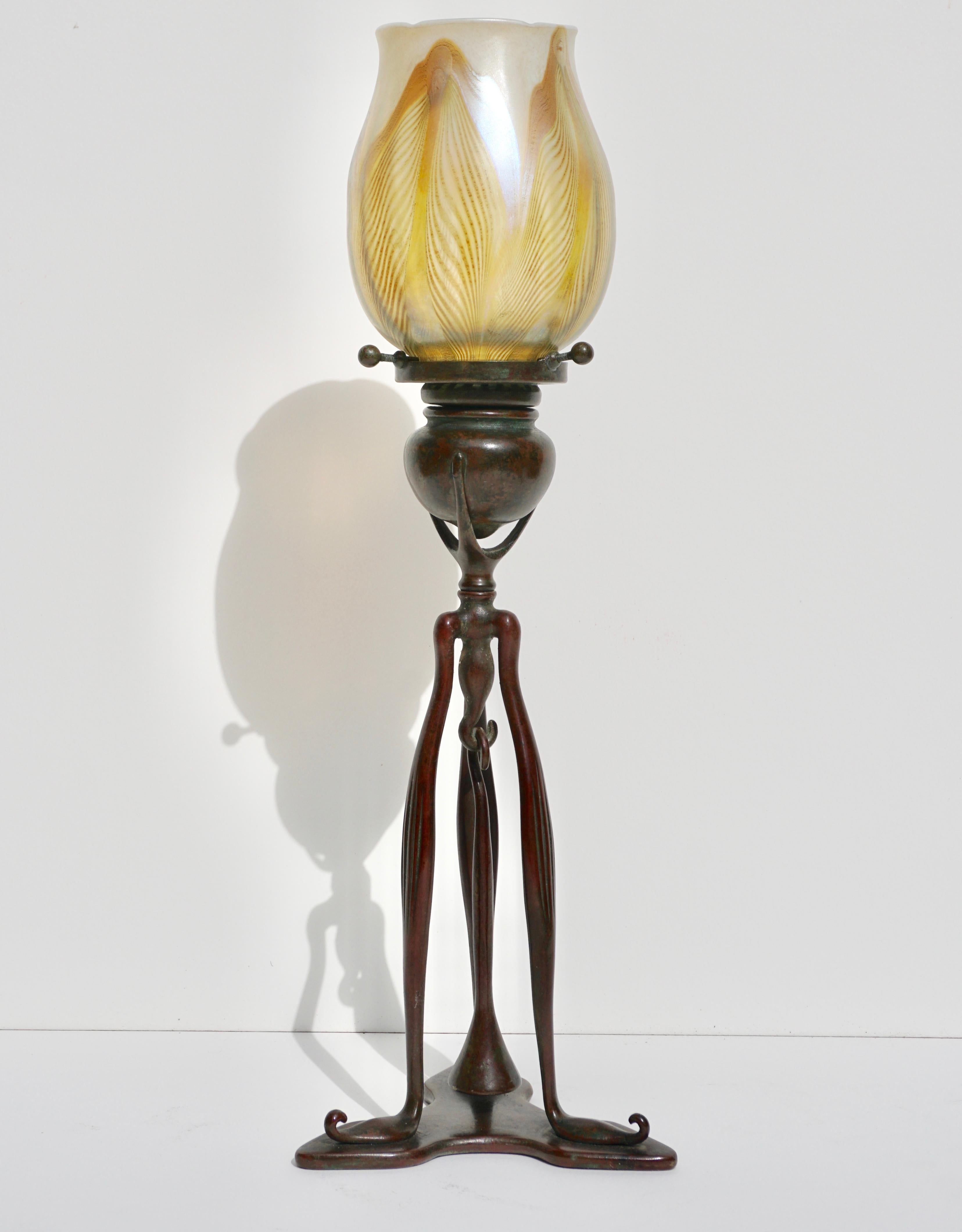 A beautiful Tiffany Studios New York 1212 Art Nouveau circa 1900 patinated bronze three legged candelabra with snuffer. With asssociated LCT Favrile pulled feather glass shade in colors or gold, green, white and yellow.

Candle stick marked