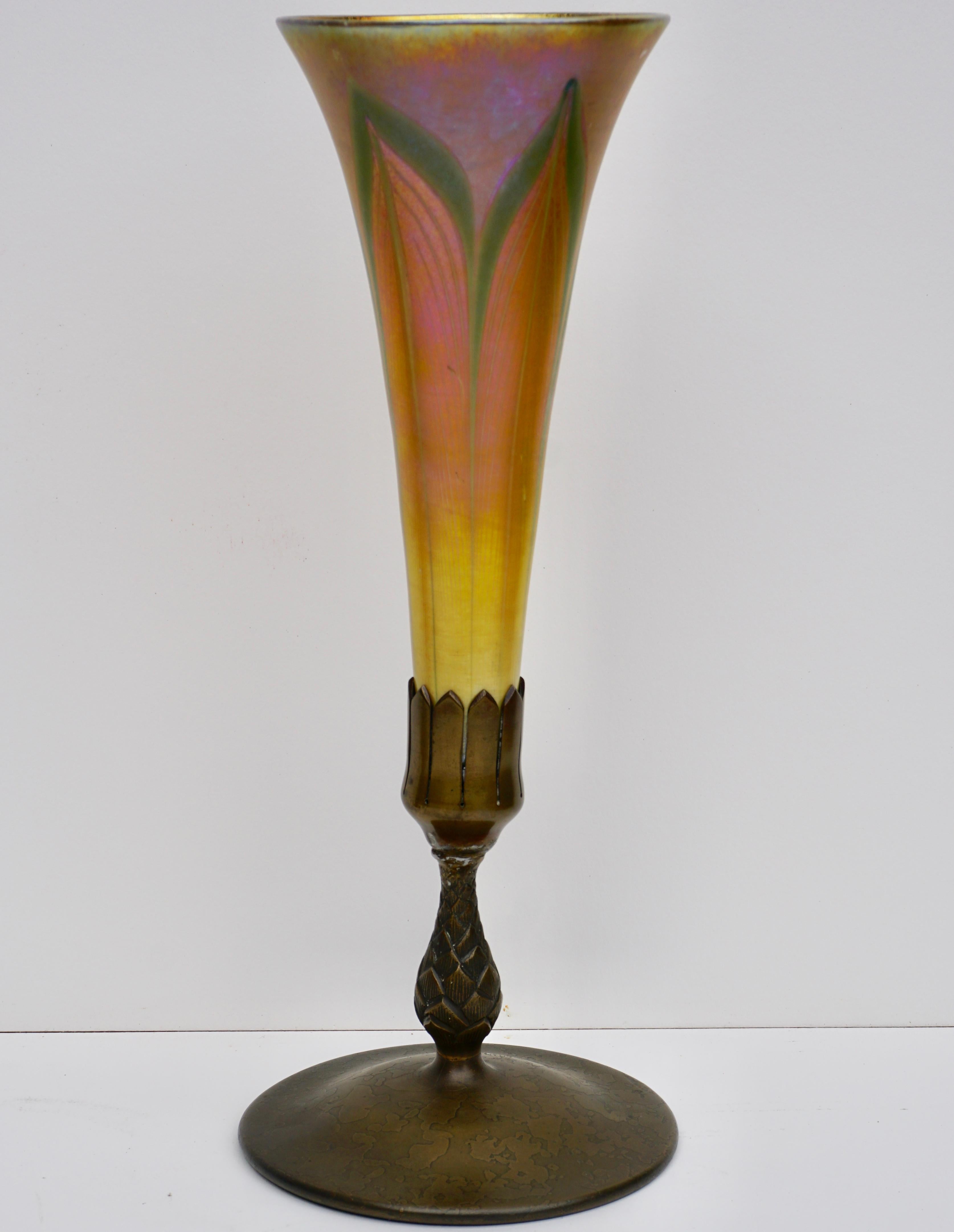 The gold trumpet-form green and white feather pulled favrile glass upper vase marked L.C.T. sitting on a bronze base with a pineapple stem and circular foot, circa 1900.

Base marked Tiffany Studios NEW YORK and numbered 1043. Monogrammed