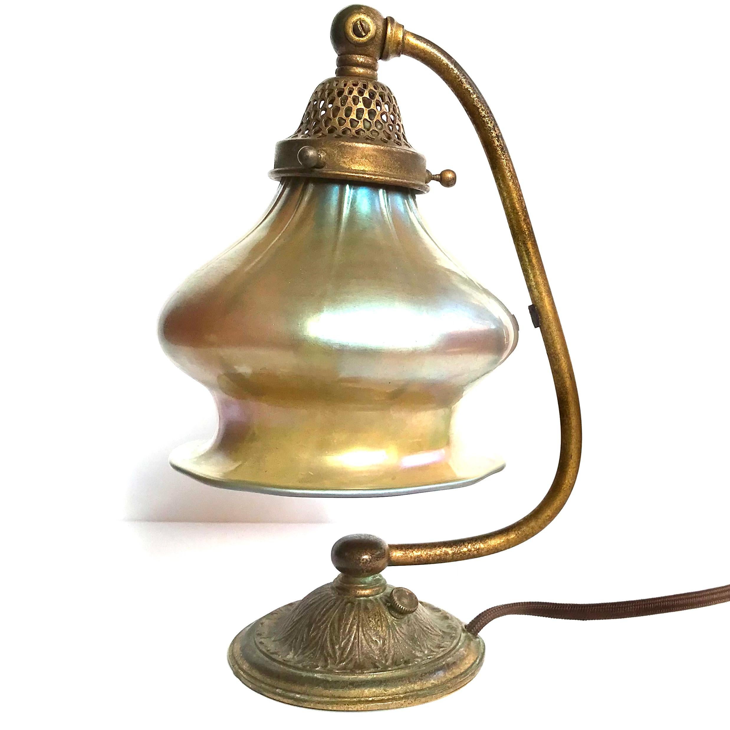 Tiffany Studios Bronze And Favrile Glass Table Lamp.
Circa 1915, period Art Nouveau Art Deco 
Gilt textured bronze and Iridescent favrile glass
Height: 10.75 Inches X 7.5 Inches
Shade: 6. Inch diameter
Base impressed: “TIFFANY STUDIOS NEW YORK