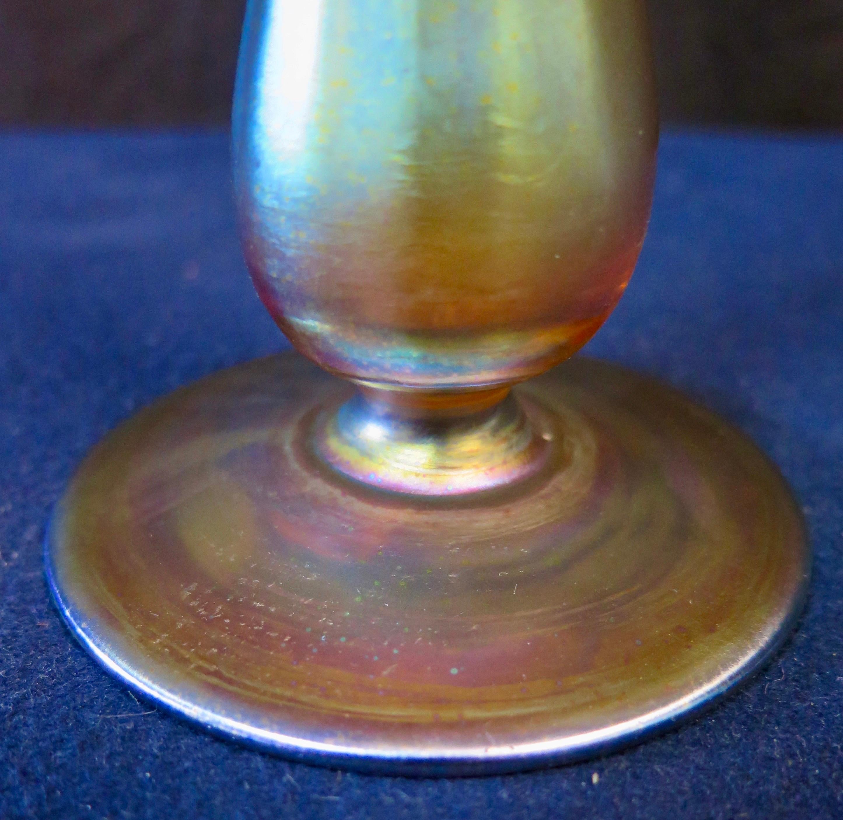 This stylish & artistic Tiffany Studios, New York bud vase is beautifully designed in brilliant iridescent favrile art glass. The vase has a sturdy round base, from which a tall slender cylinder rises culminating in a vivid bold lip. The