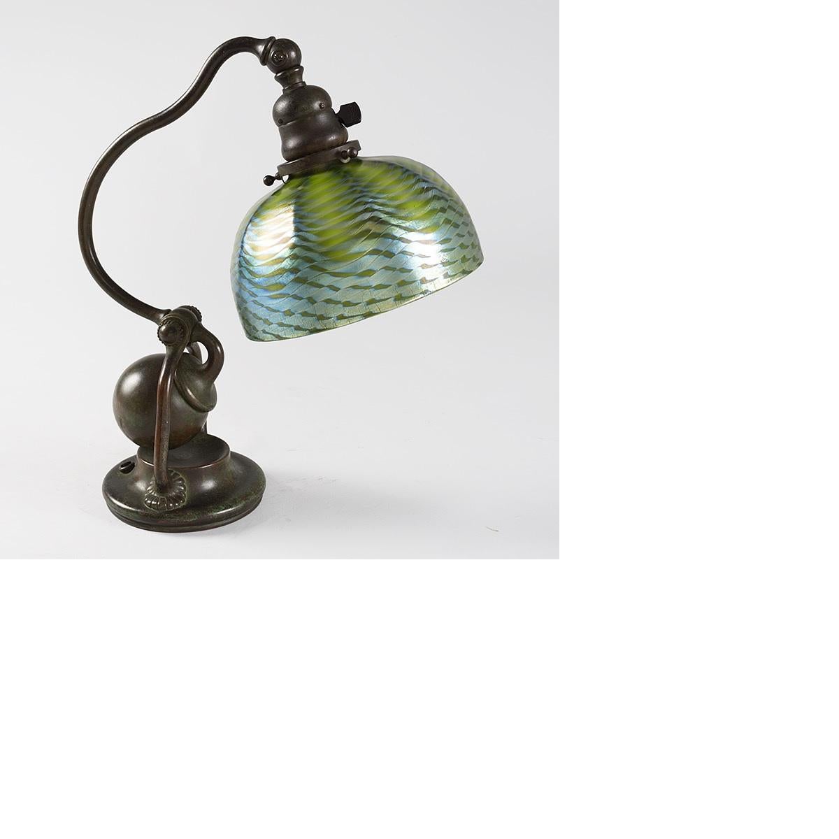 A Tiffany Studios New York glass and bronze “Counter Balance” desk lamp, featuring a blue and green iridescent “Damascene” Favrile glass shade suspended from a patinated bronze base.  Circa 1900.

Pictured in ‘“Tiffany Lamps and Metalware, An